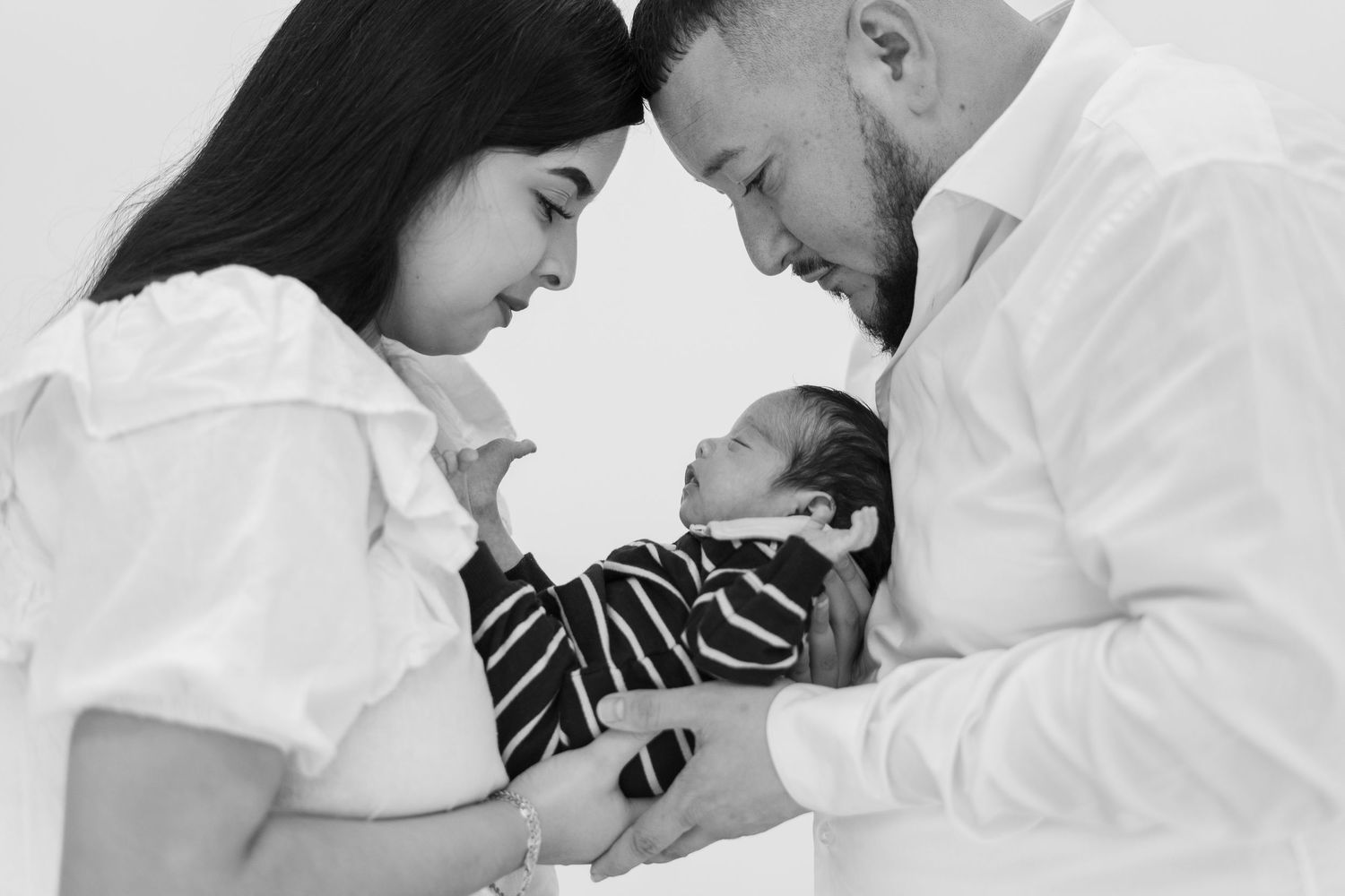 Black and white portrait of parents lovingly gazing at their newborn baby.