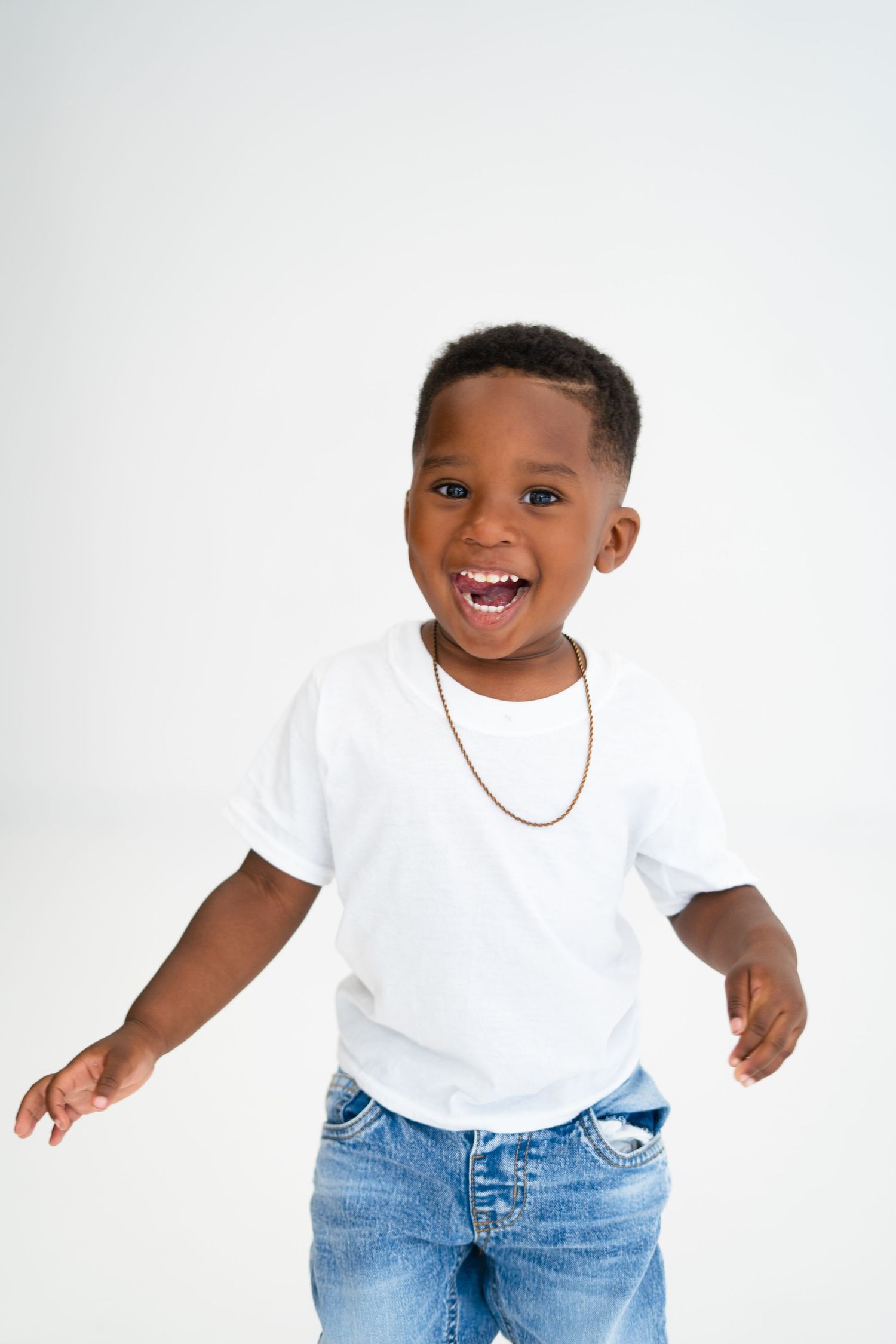 Joyful Black toddler boy laughing in white t-shirt and jeans against a white background.
