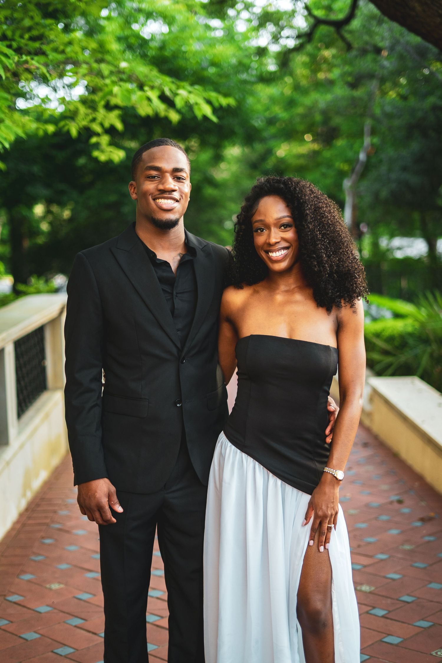 Smiling Black couple posing together on brick pathway in coordinated black and white outfits.