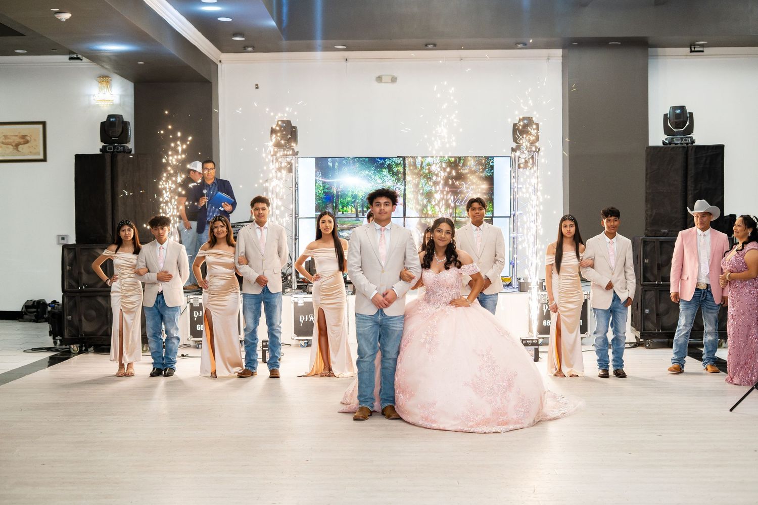 A quinceañera court in pink and white formal attire poses on the dance floor.