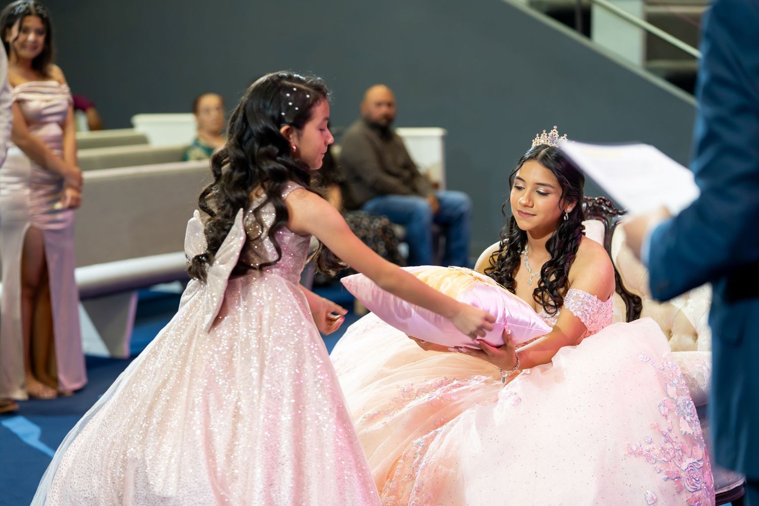 Two girls in pink quinceañera gowns sharing a tender moment during a formal celebration ceremony.