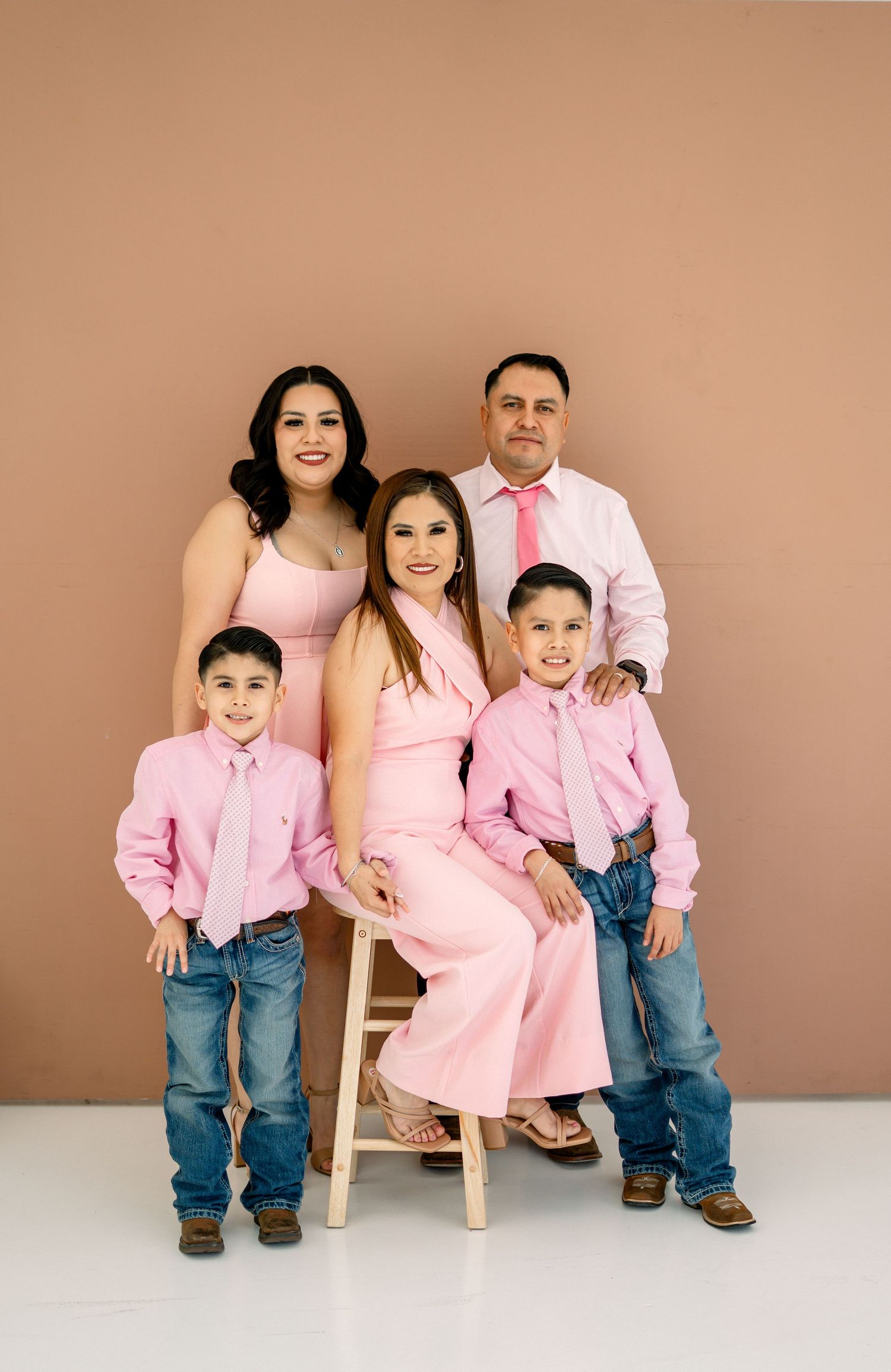 Family of five in coordinating pink outfits posing for a studio portrait.
