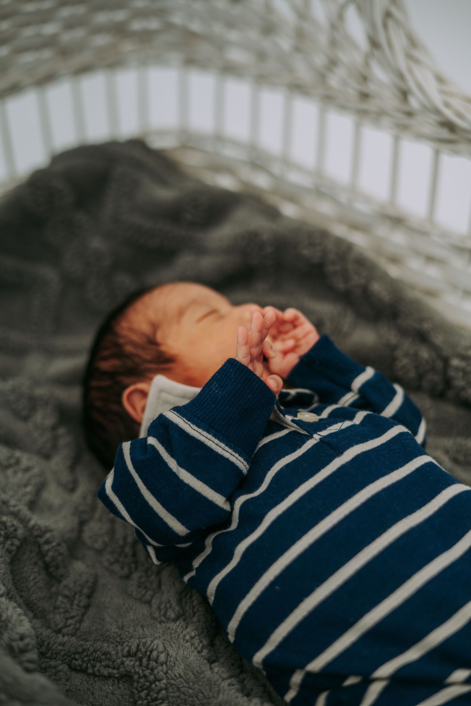 Sleeping newborn baby in blue striped onesie lying in white crib on gray blanket.