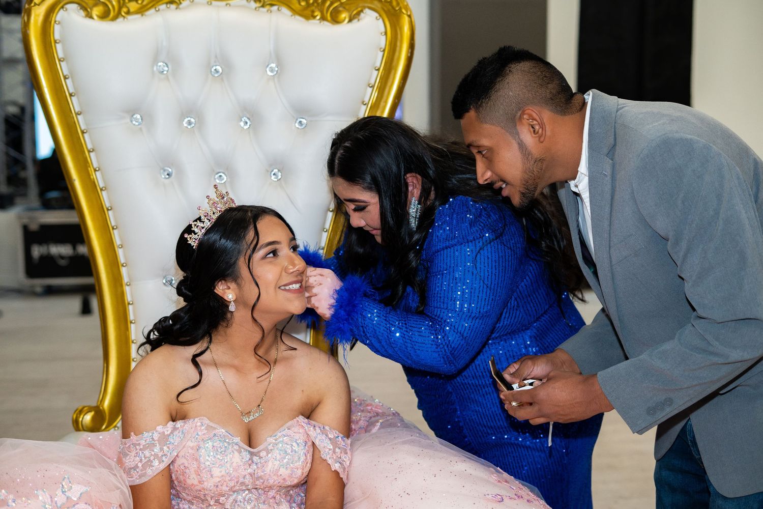 Family members lovingly attend to a quinceañera seated on a gold throne chair.