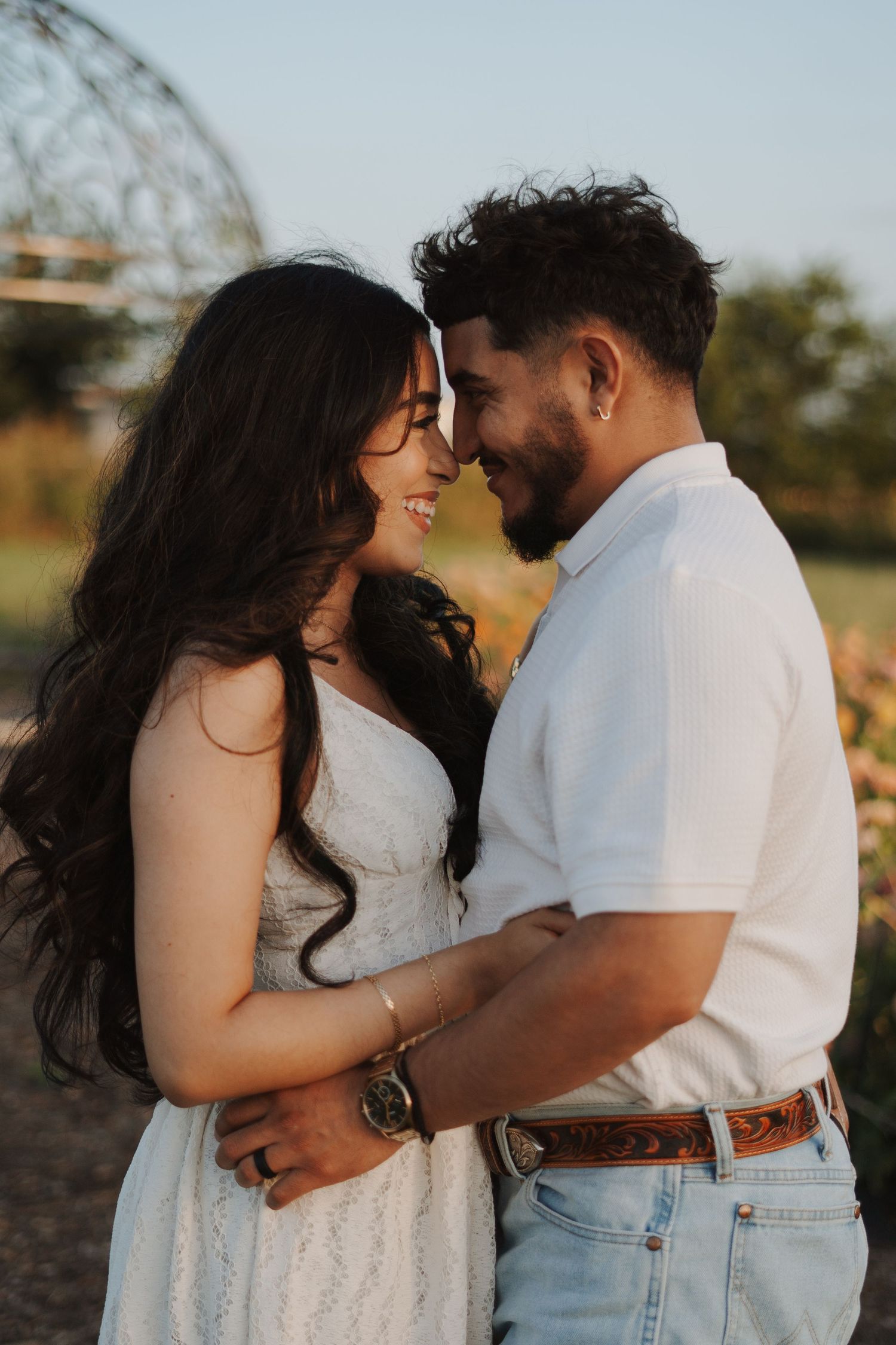 A couple in white outfits share a romantic forehead touch outdoors in golden hour light.