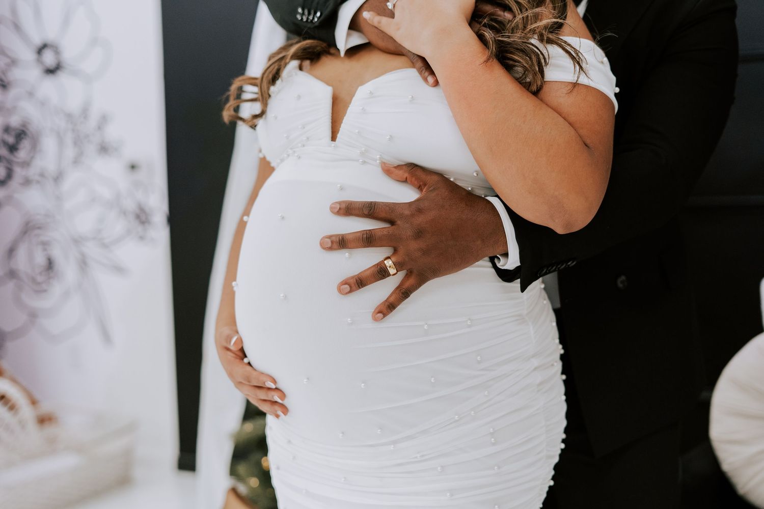 Close-up of couple embracing pregnant belly, showing diamond ring, in elegant black and white attire.