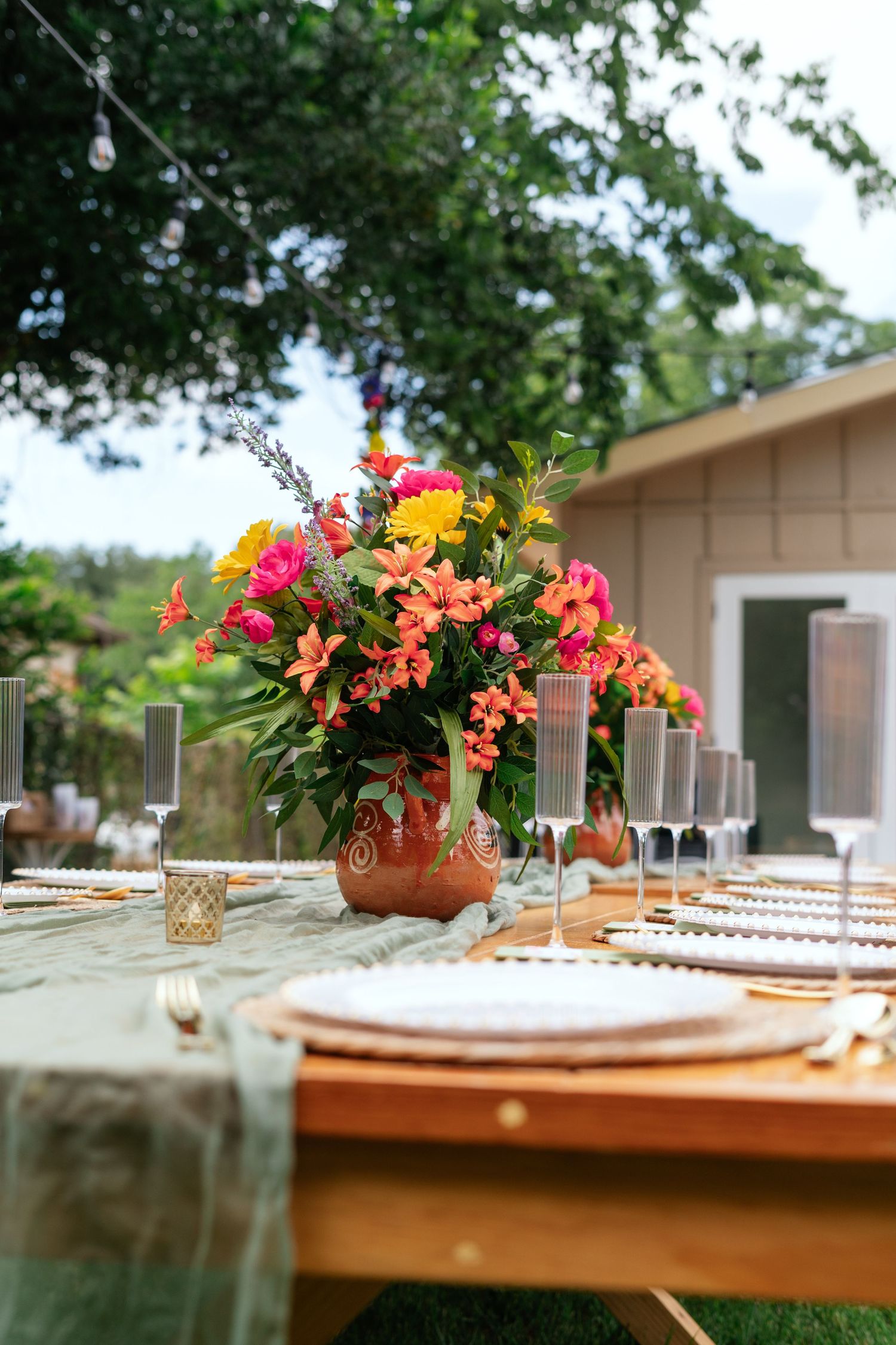 Elegant outdoor dining table with colorful floral centerpiece, champagne flutes, and place settings.