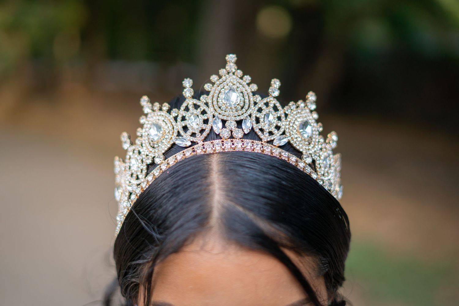 Close-up of an ornate silver crystal and rhinestone tiara crown on dark hair outdoors.