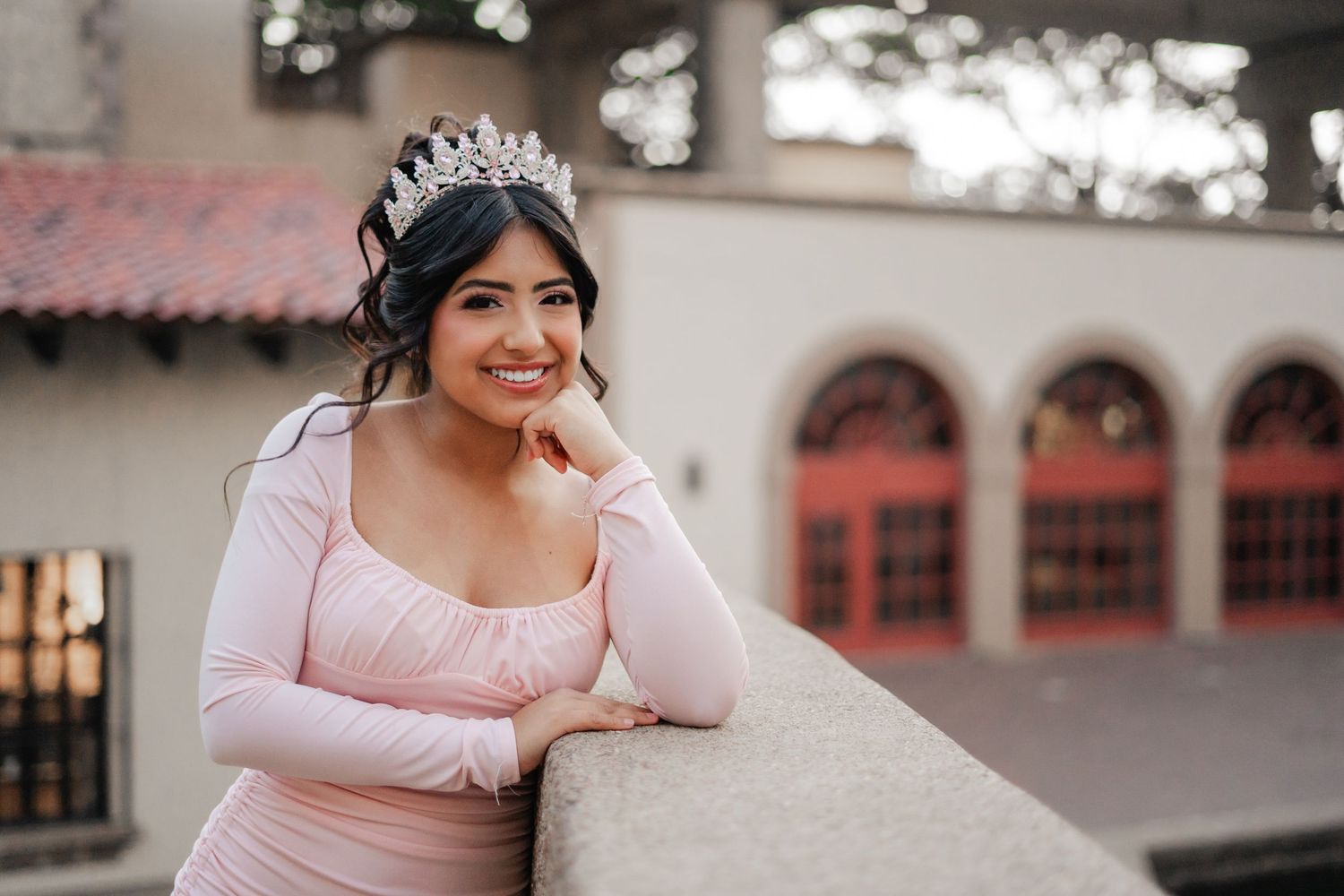 Young woman in pink dress and tiara smiling at quinceanera photo shoot at elegant venue.