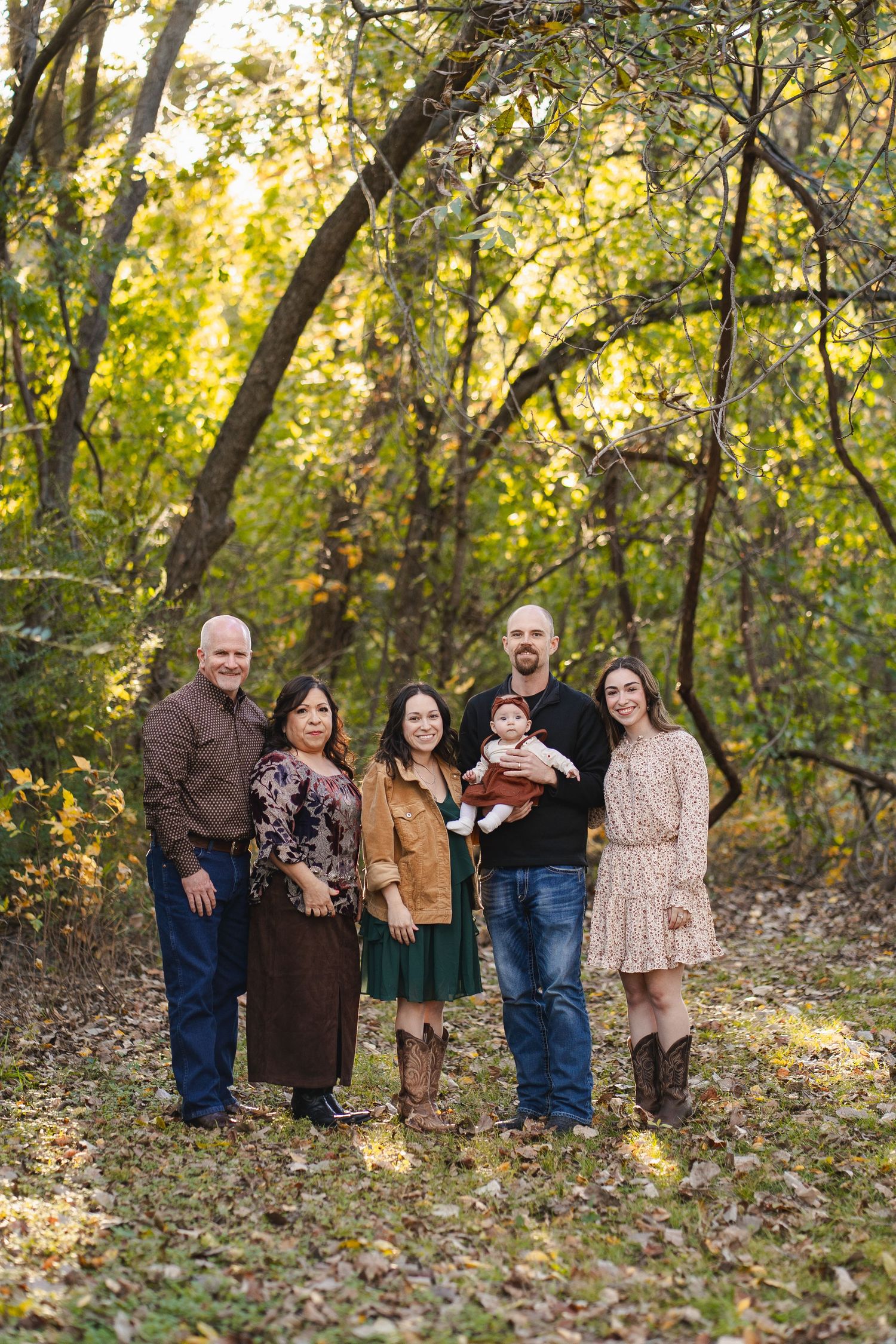 Extended family of six posing together in a sunlit forest with vibrant autumn foliage.
