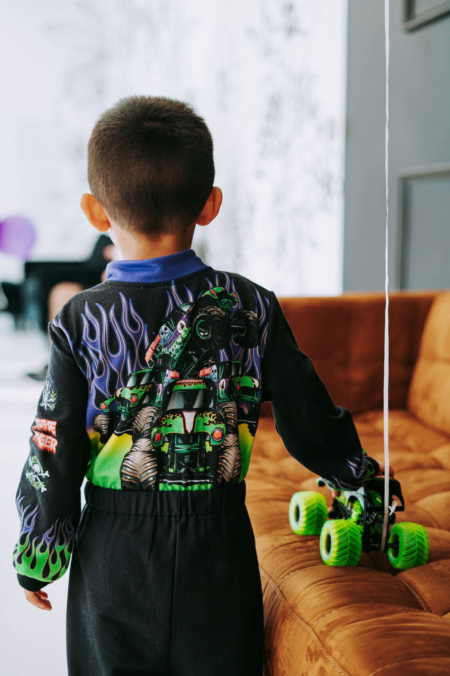 Boy in Grave Digger outfit standing by number 4 balloon celebrating 4th birthday with monster trucks.