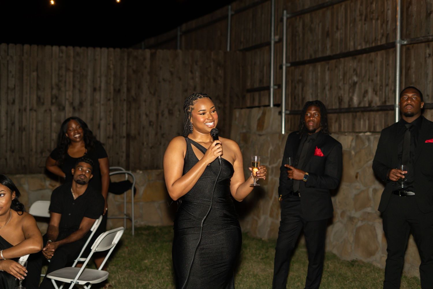 Group of guests in black attire gathered at an outdoor evening wedding reception celebration.
