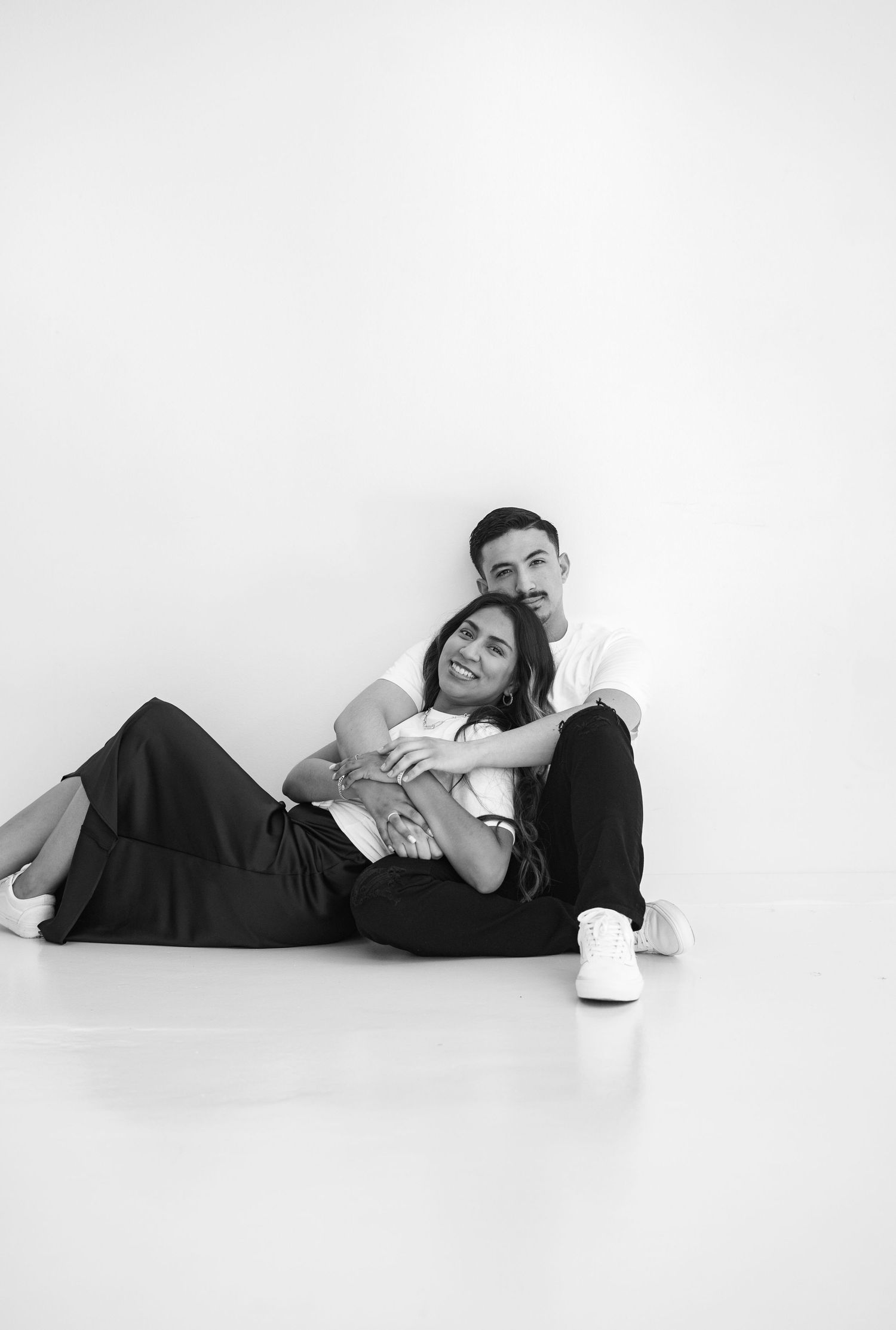 Black and white photo of couple sitting on floor, woman reclining on mans lap tenderly.