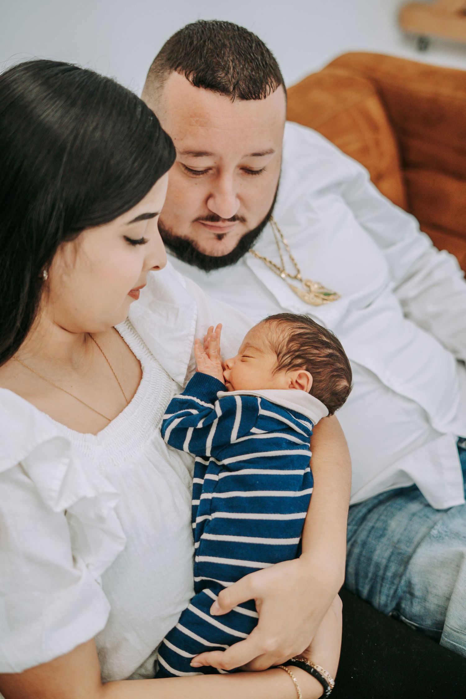 A couple tenderly looks at their newborn baby dressed in a blue striped outfit.