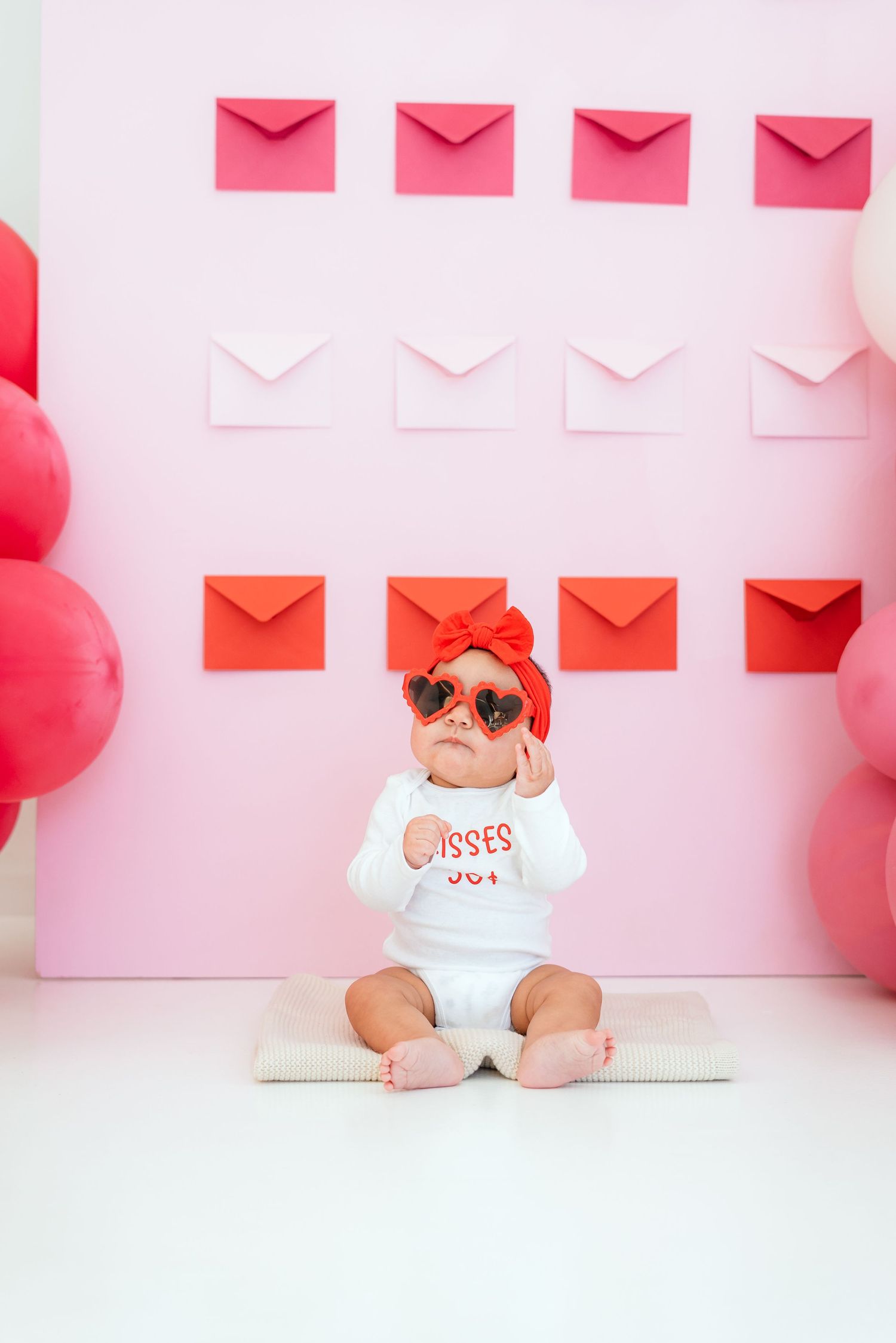 Baby in heart sunglasses wearing 'Kisses 50 cents' onesie with envelope backdrop.