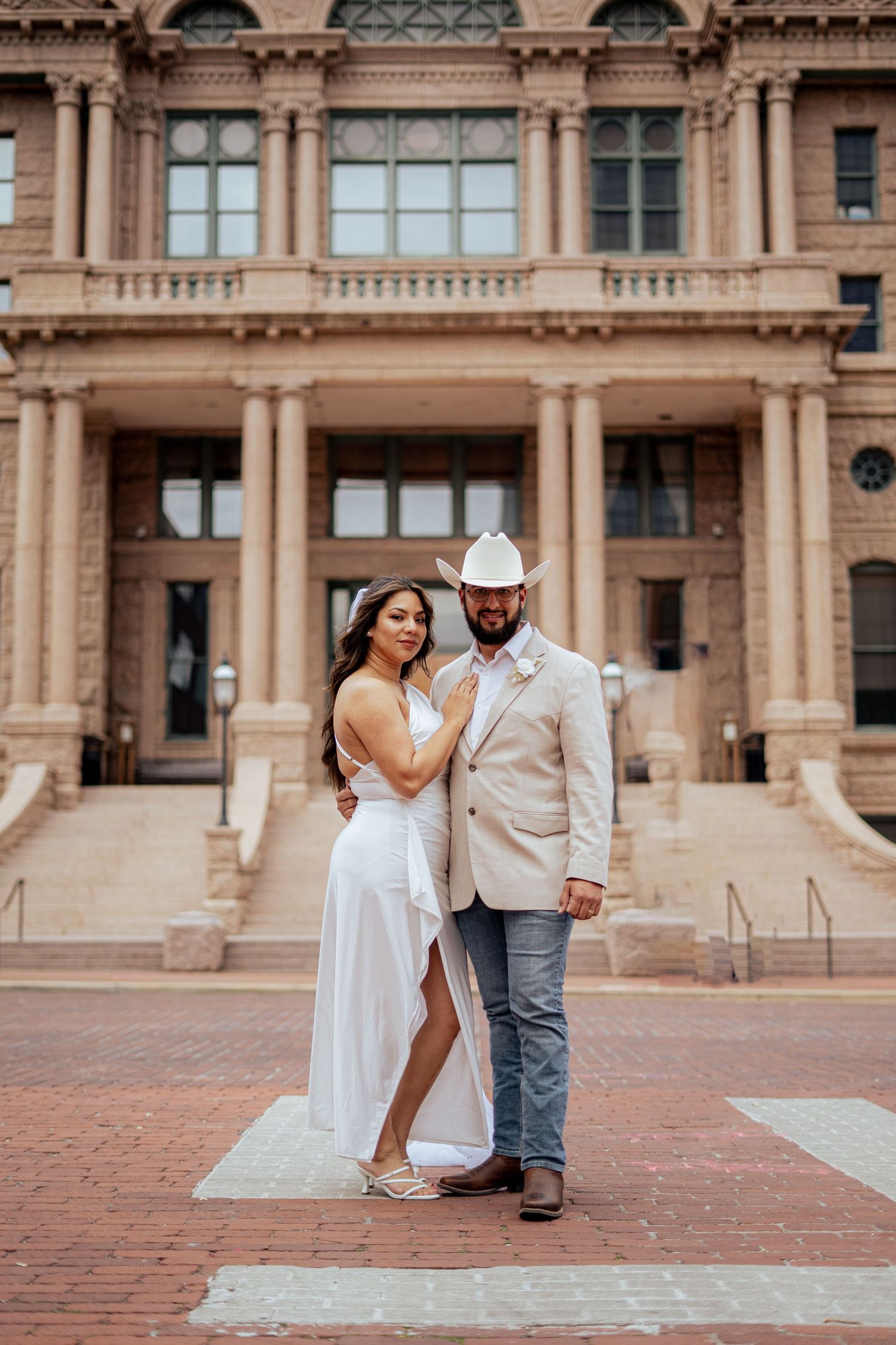 Bride and groom pose in front of a grand historic building on their Texas courthouse wedding day.