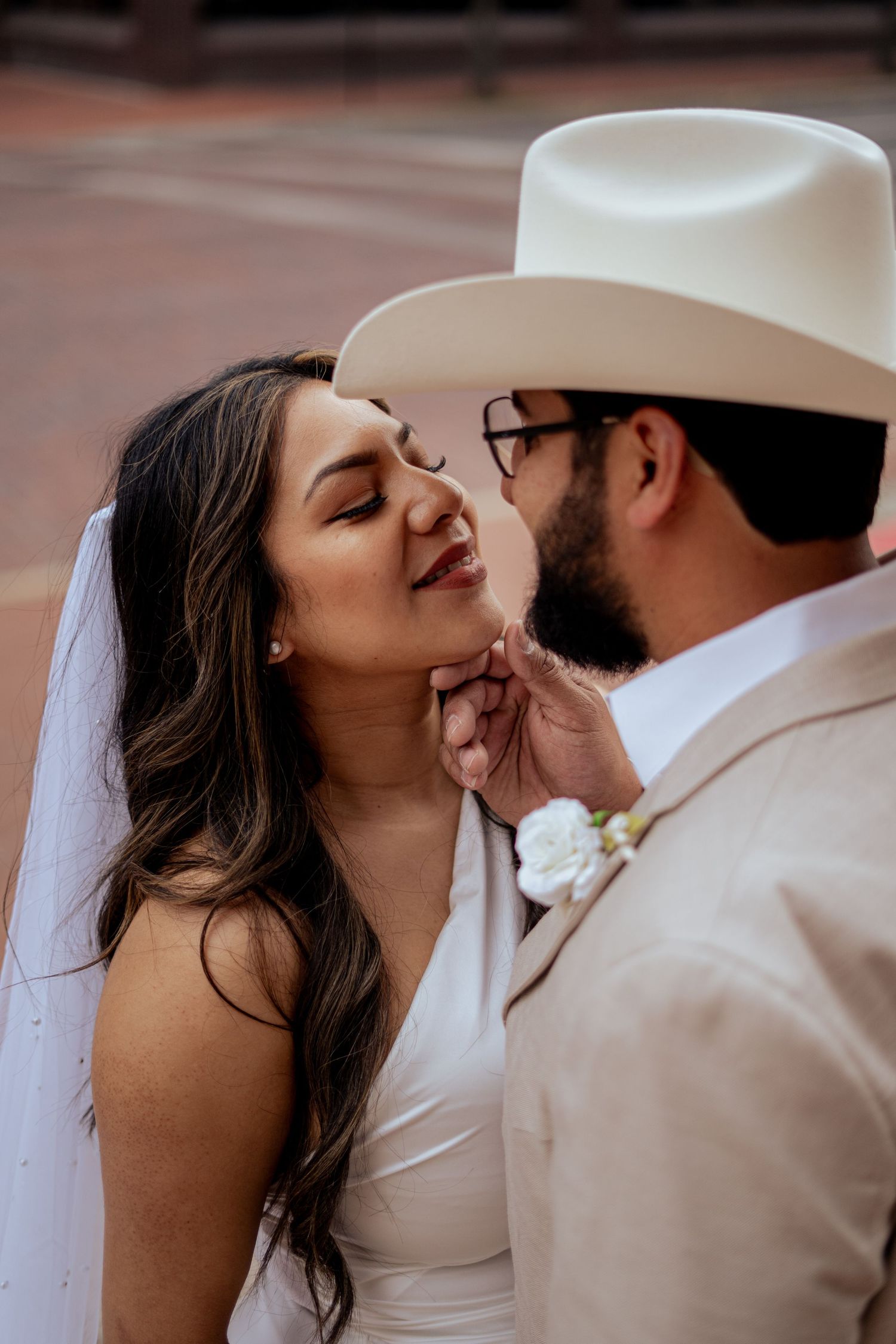 Groom in white cowboy hat gently lifts bride's chin for a kiss during outdoor wedding portraits.