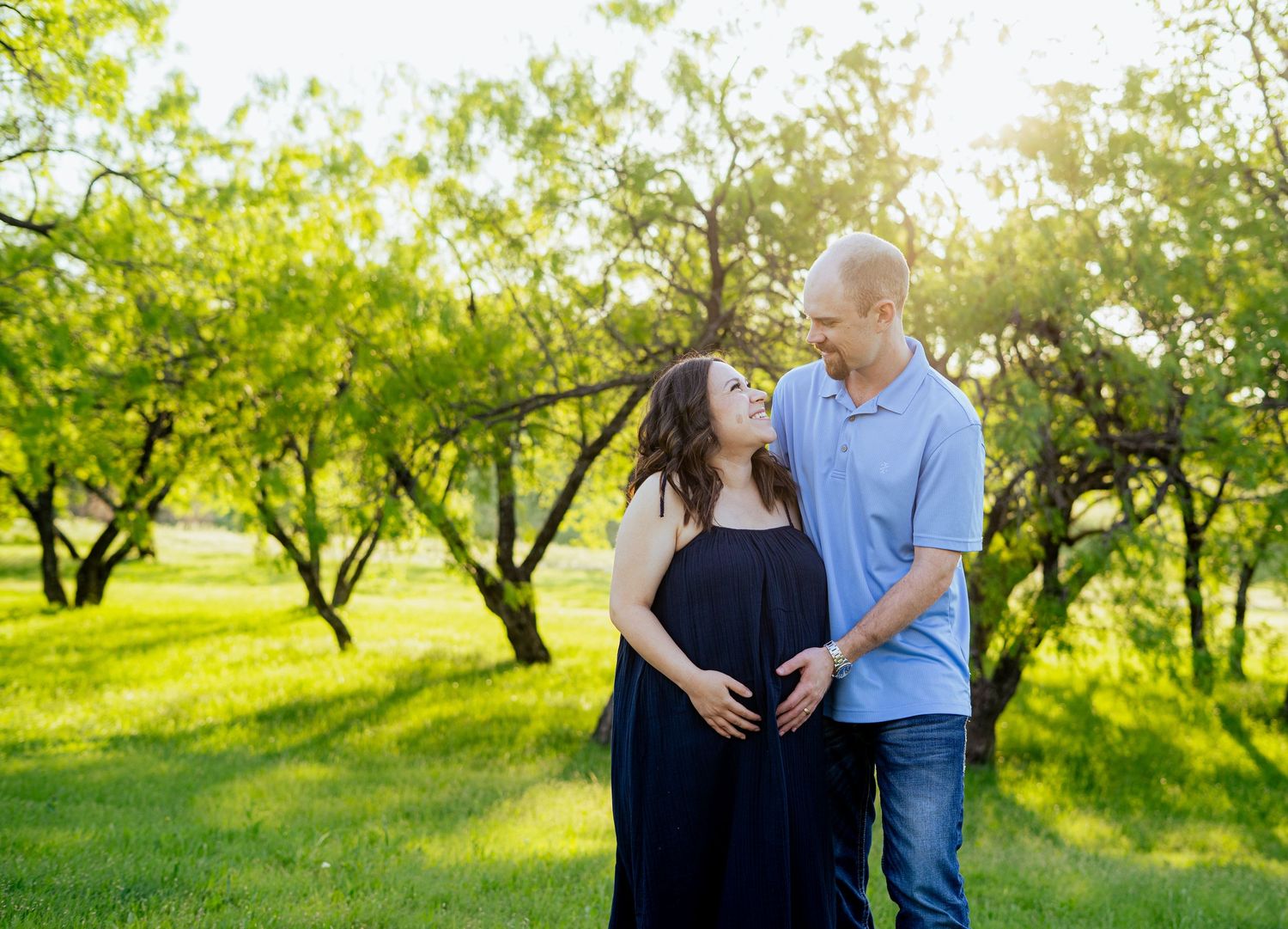 Expecting couple sharing a loving glance in a sunlit green park during maternity photo session.