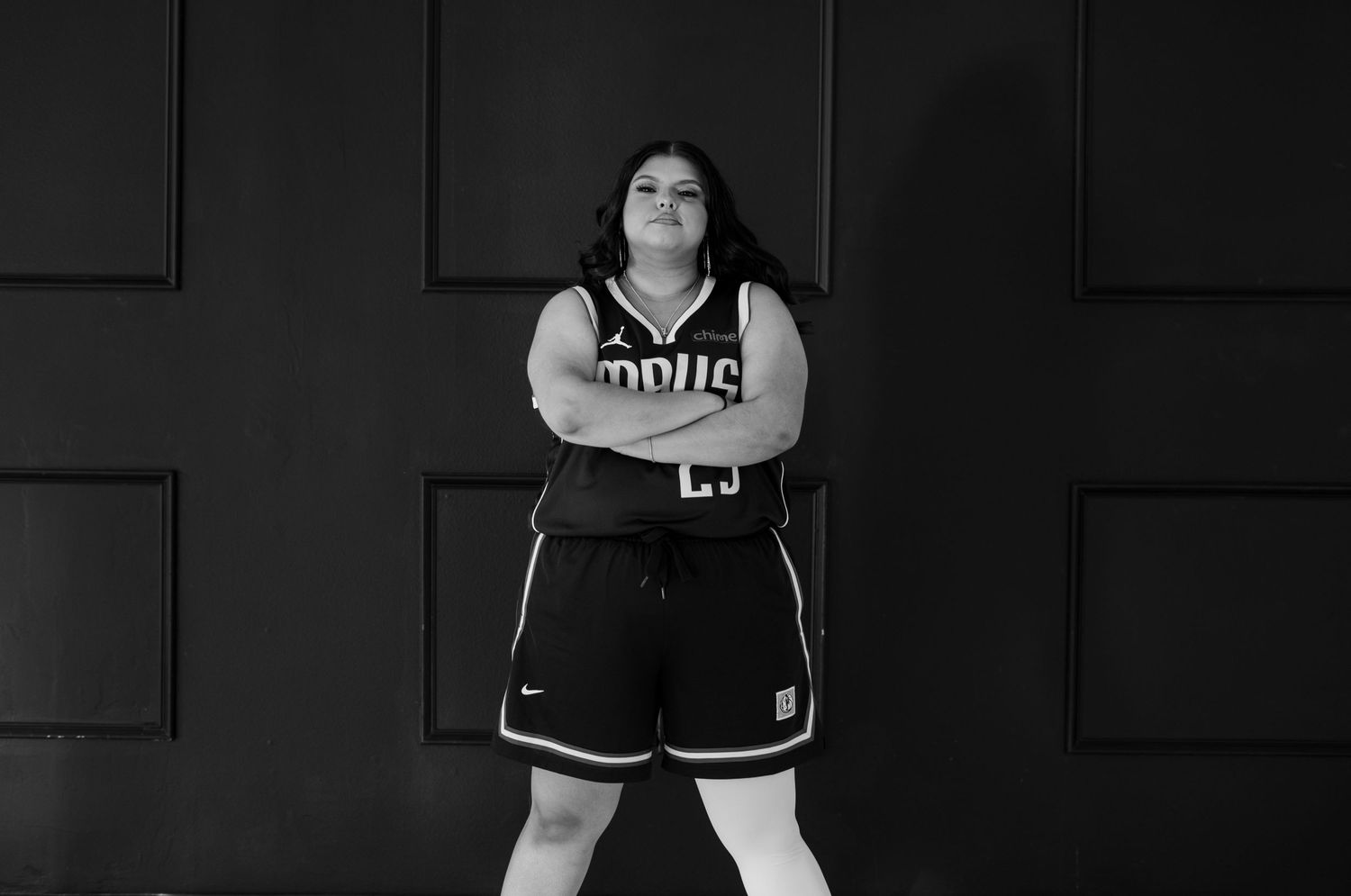 Black and white photo of woman in Mavericks jersey posing with arms crossed in studio.