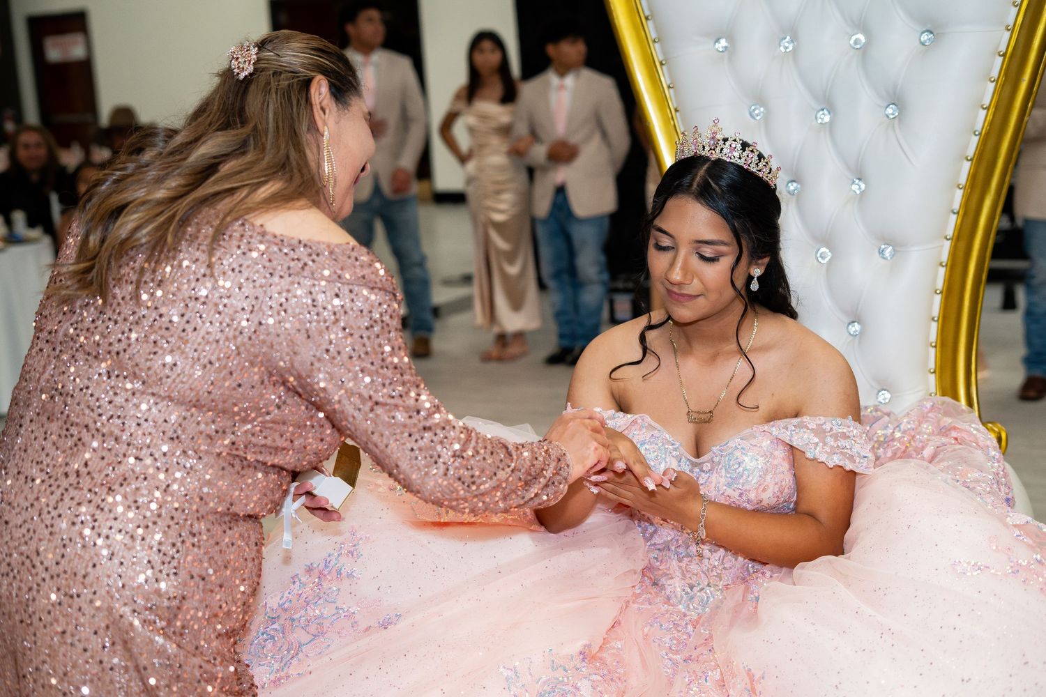 A mother places a ring on her daughters hand during a quinceañera ceremony.