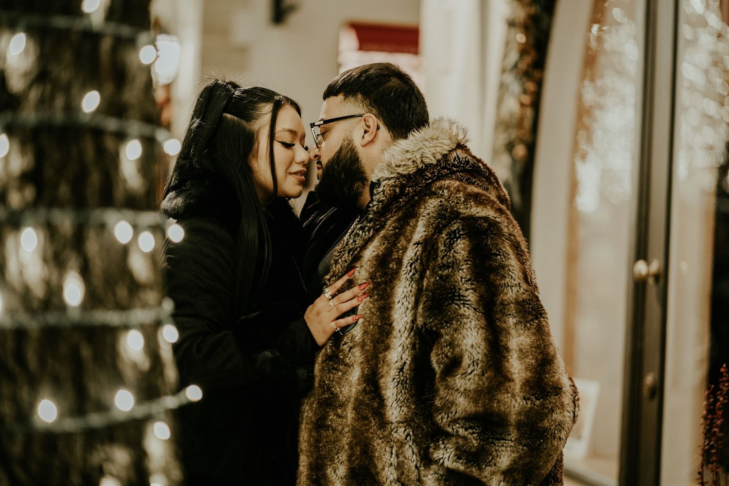 Romantic couple sharing an intimate moment near a glowing Christmas tree at night outdoors.