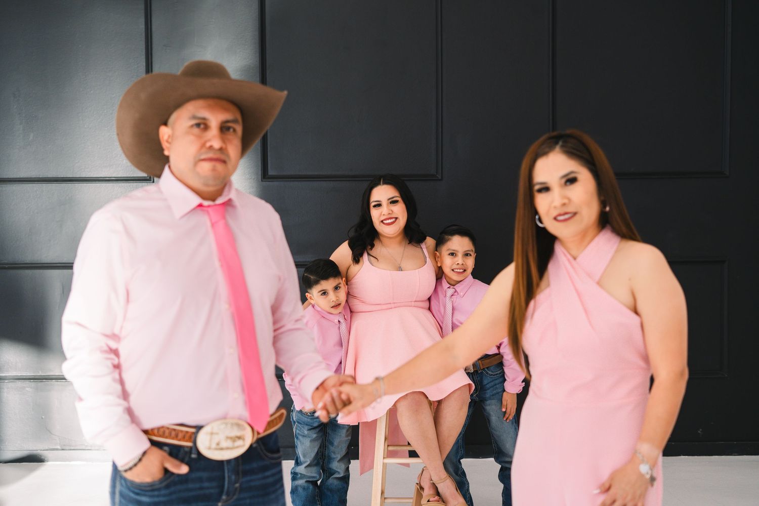 A family in coordinated pink outfits, including a man in a cowboy hat, pose for a studio portrait.