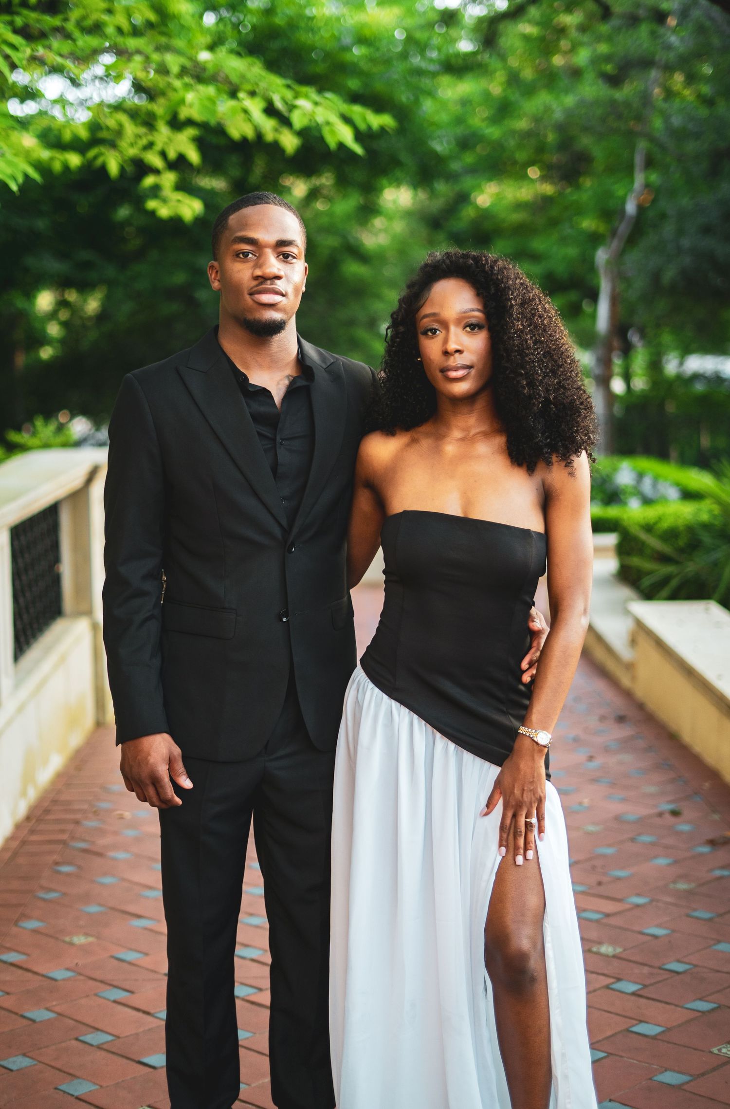 Sophisticated Black couple posing seriously on brick walkway in elegant black and white attire.