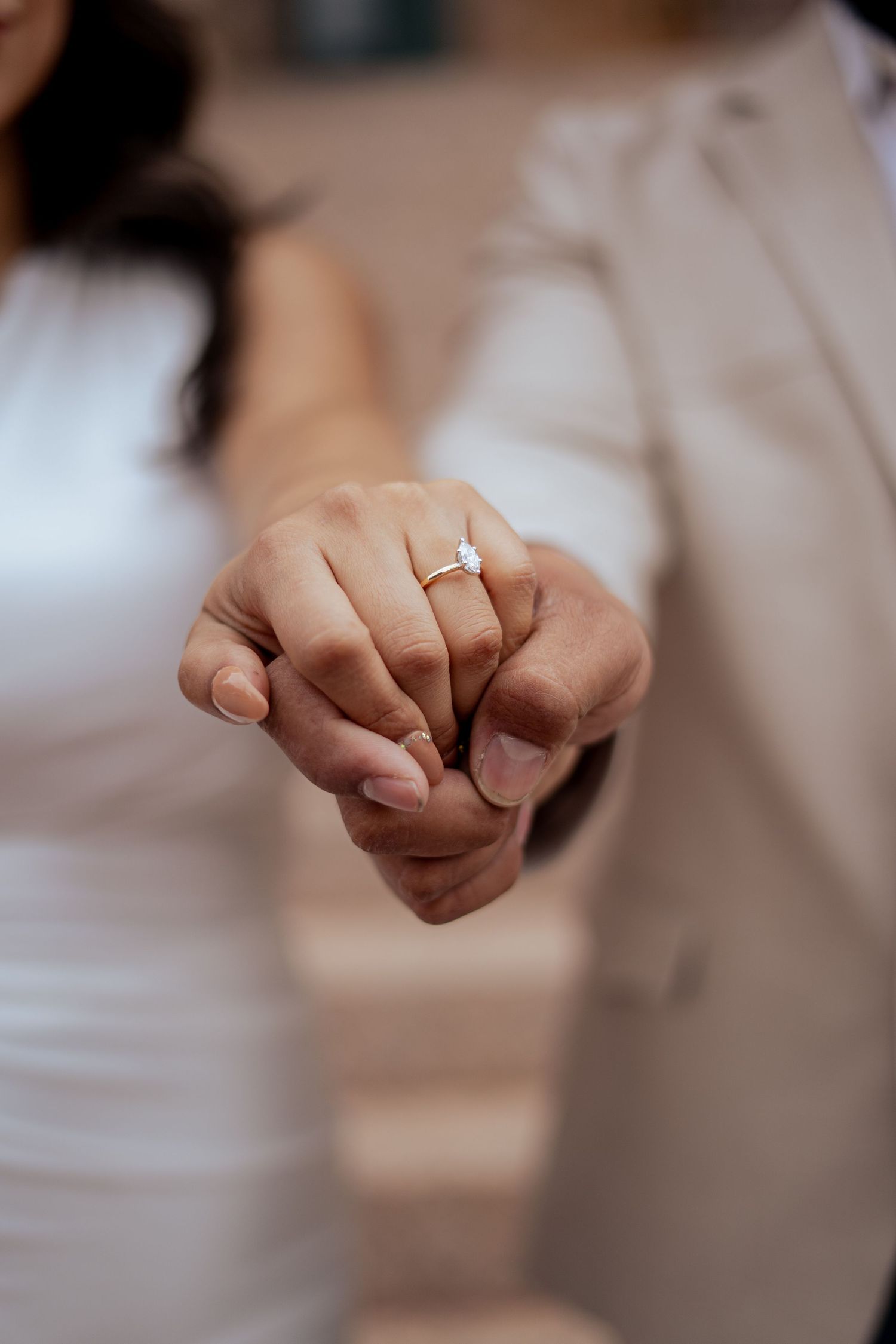 A close-up of a bride and groom holding hands showcasing a sparkling diamond engagement ring.