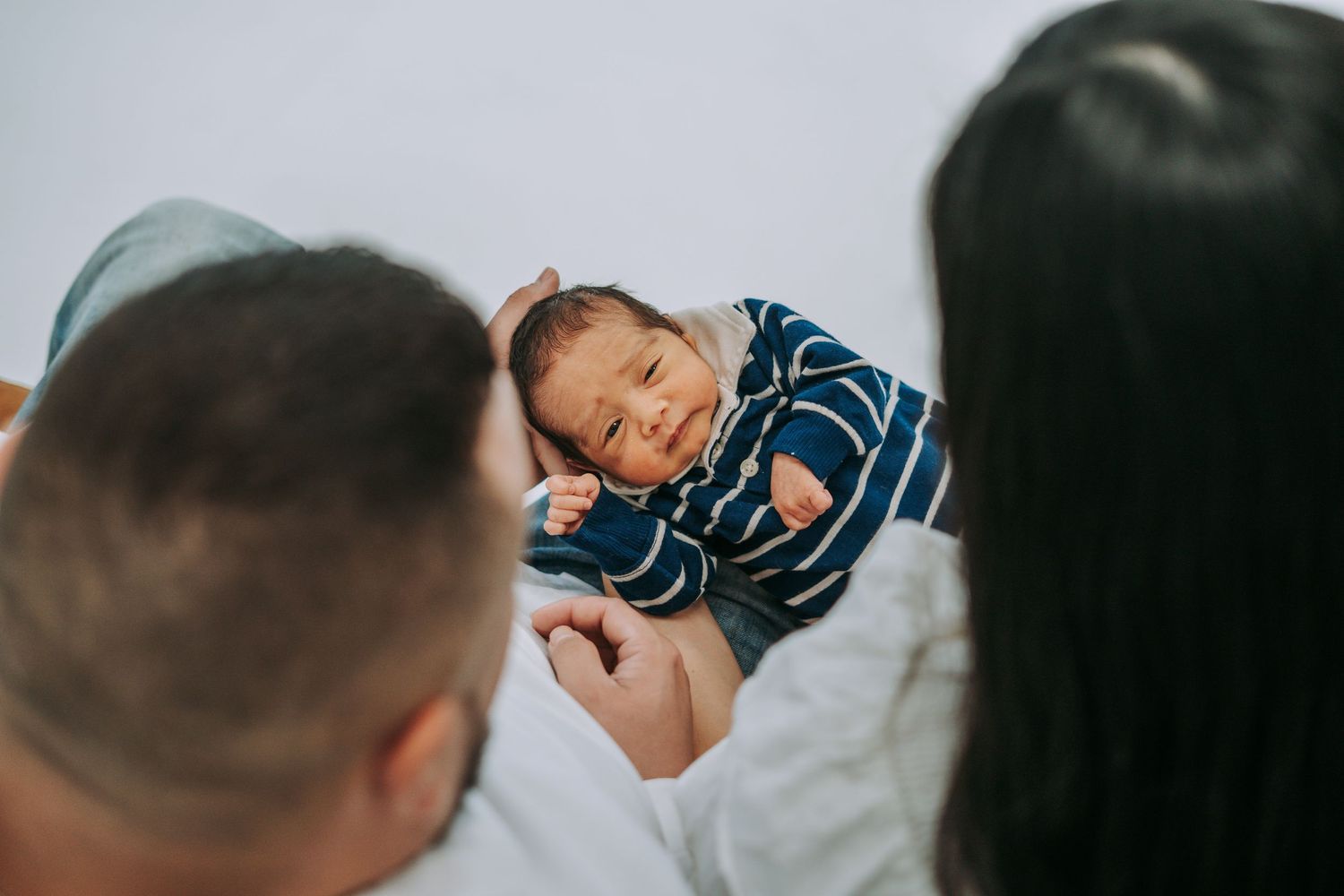 New parents lovingly gazing down at their newborn baby dressed in a blue striped outfit.