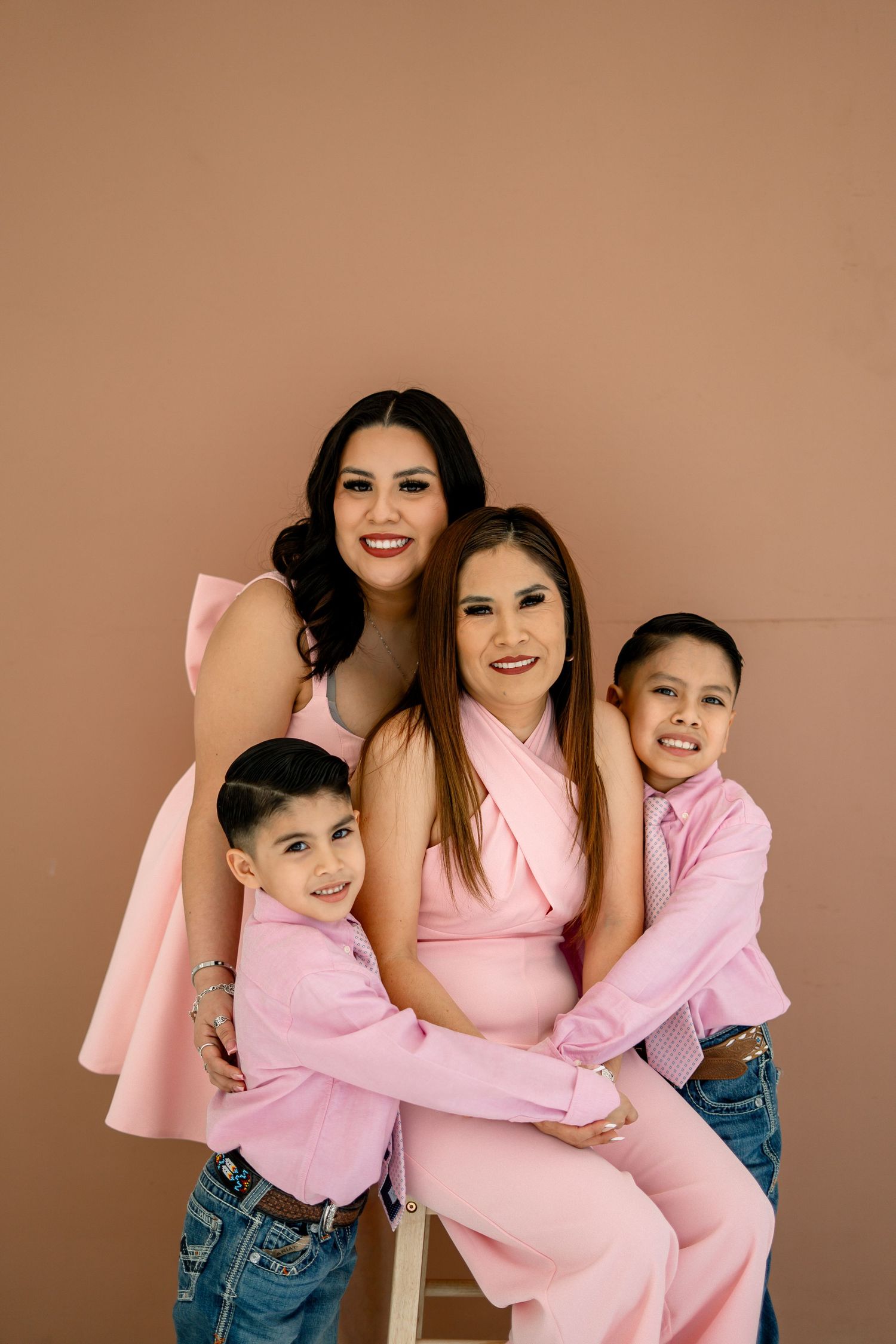 Two women and two boys in pink outfits pose together for a family portrait.