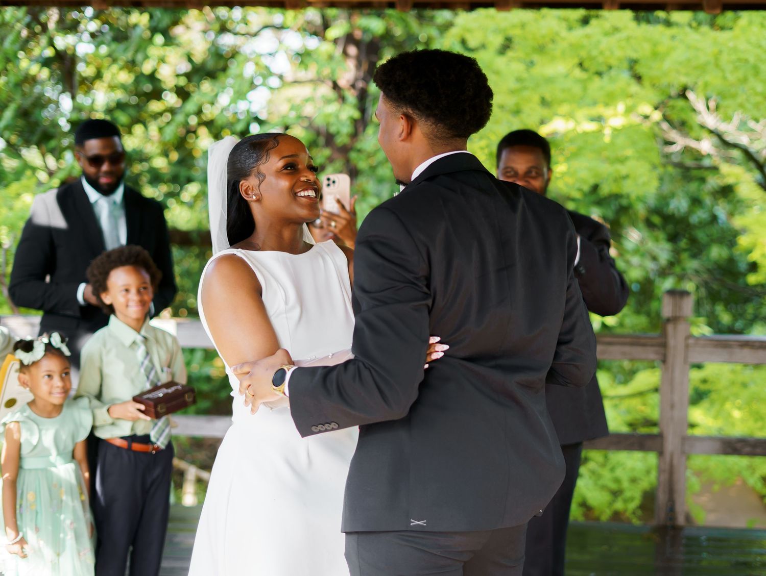 Bride and groom share a tender dance moment during outdoor wedding ceremony surrounded by family and guests.