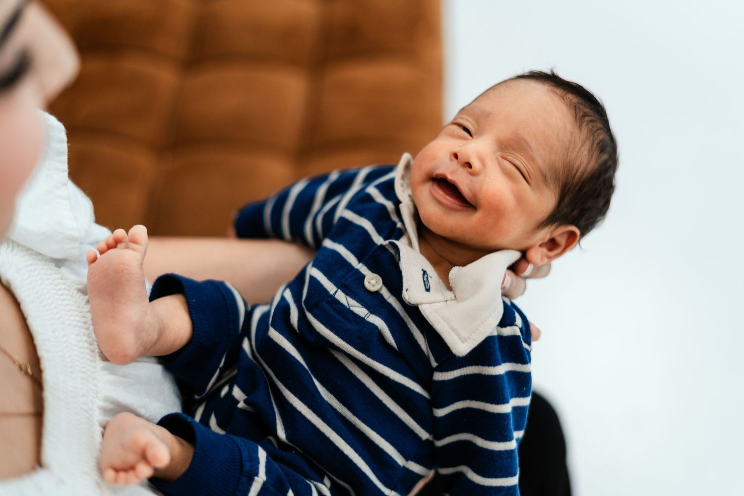 Newborn baby in a blue striped outfit smiling while being held by a parent.
