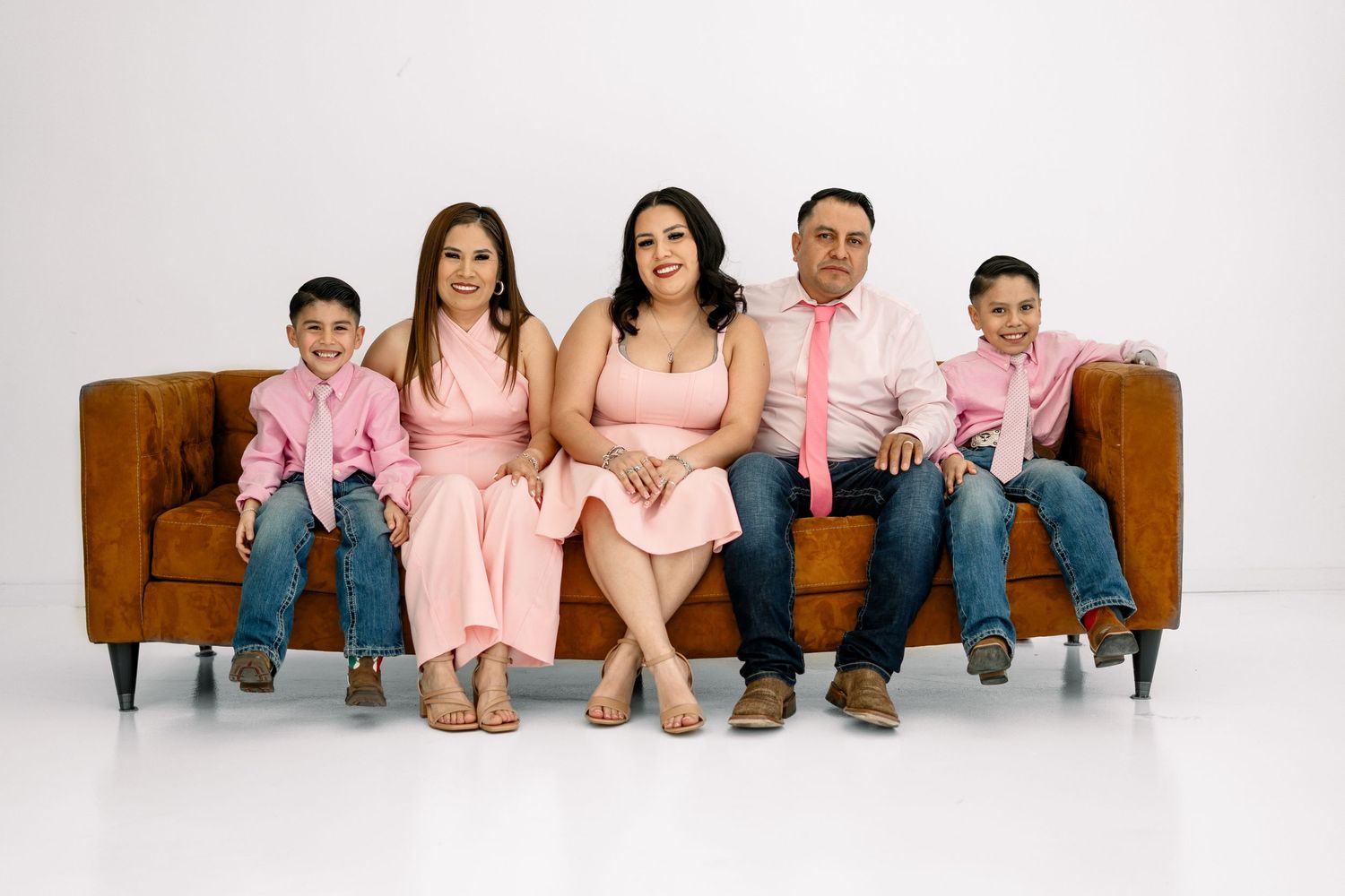 Family of five in pink outfits sitting together on a brown couch.
