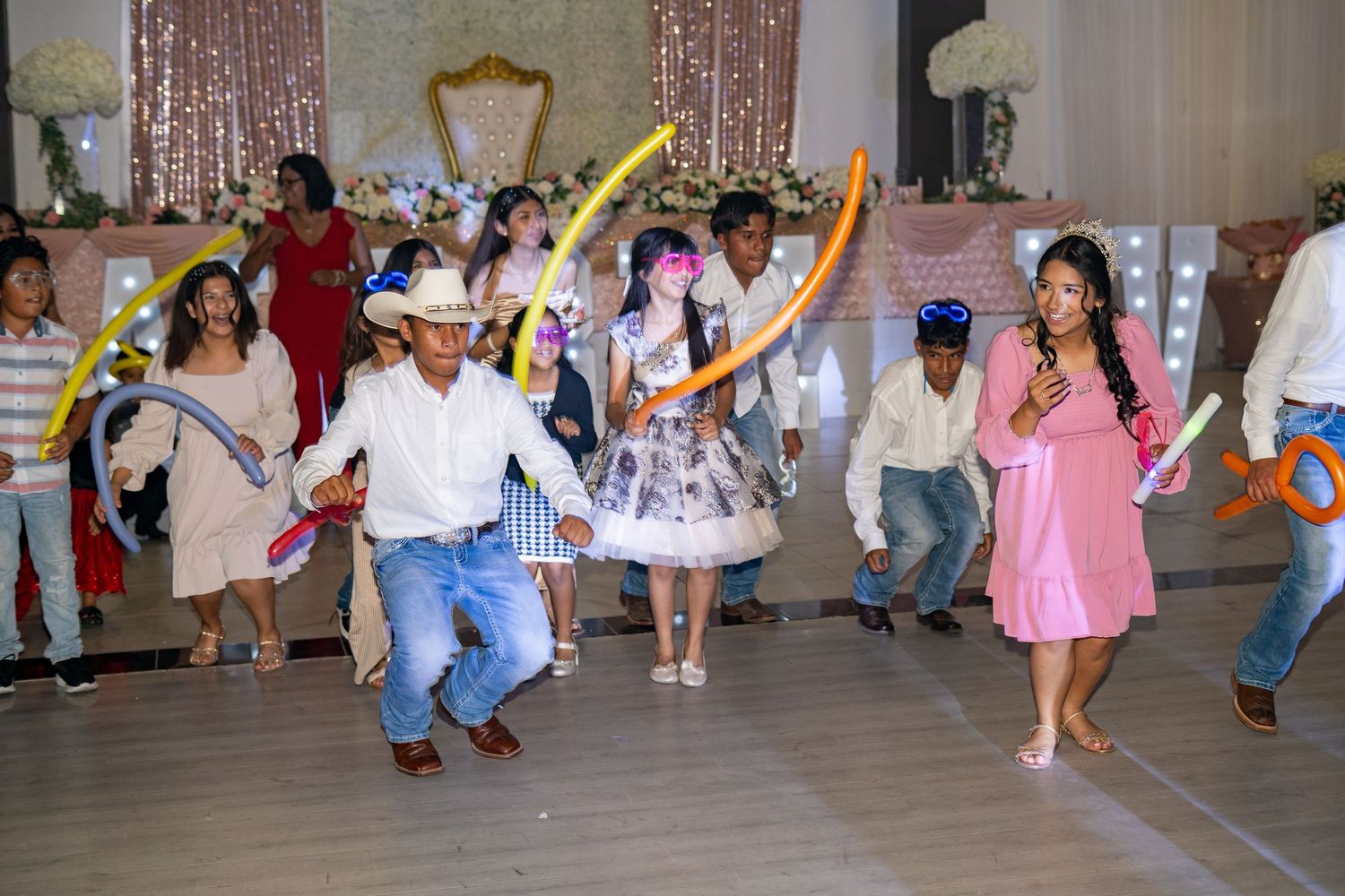 Guests dance joyfully with balloon decorations at a vibrant quinceañera party celebration indoors.