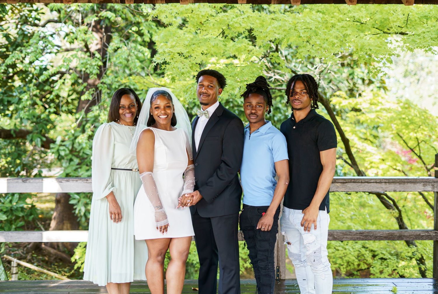 Family portrait of five people smiling together on a wooden bridge at an outdoor wedding venue.