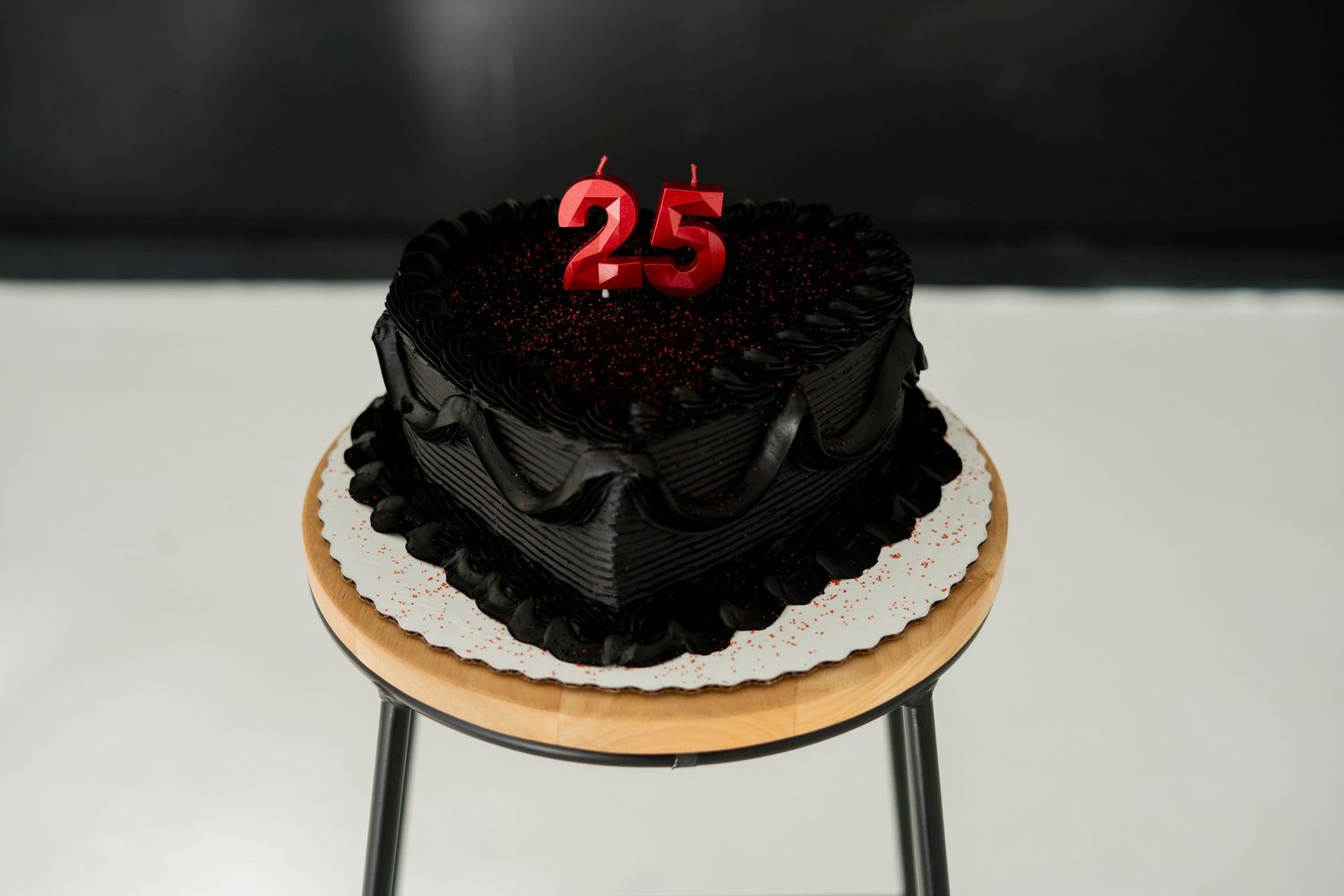 Heart-shaped chocolate birthday cake with red number 25 candles on wooden stand.