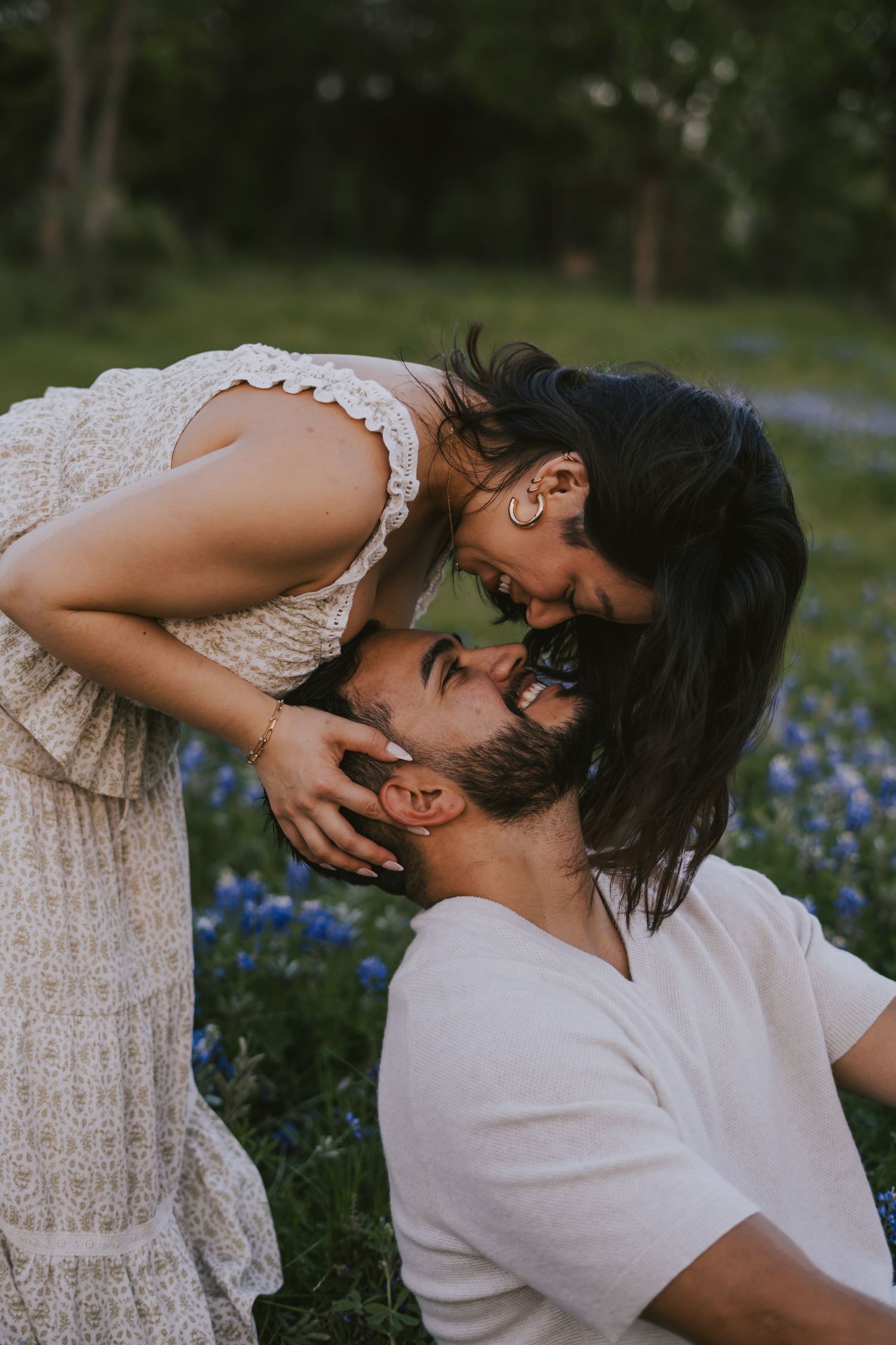 A couple shares a romantic moment in a field of blue wildflowers, with the woman leaning down to kiss the man.