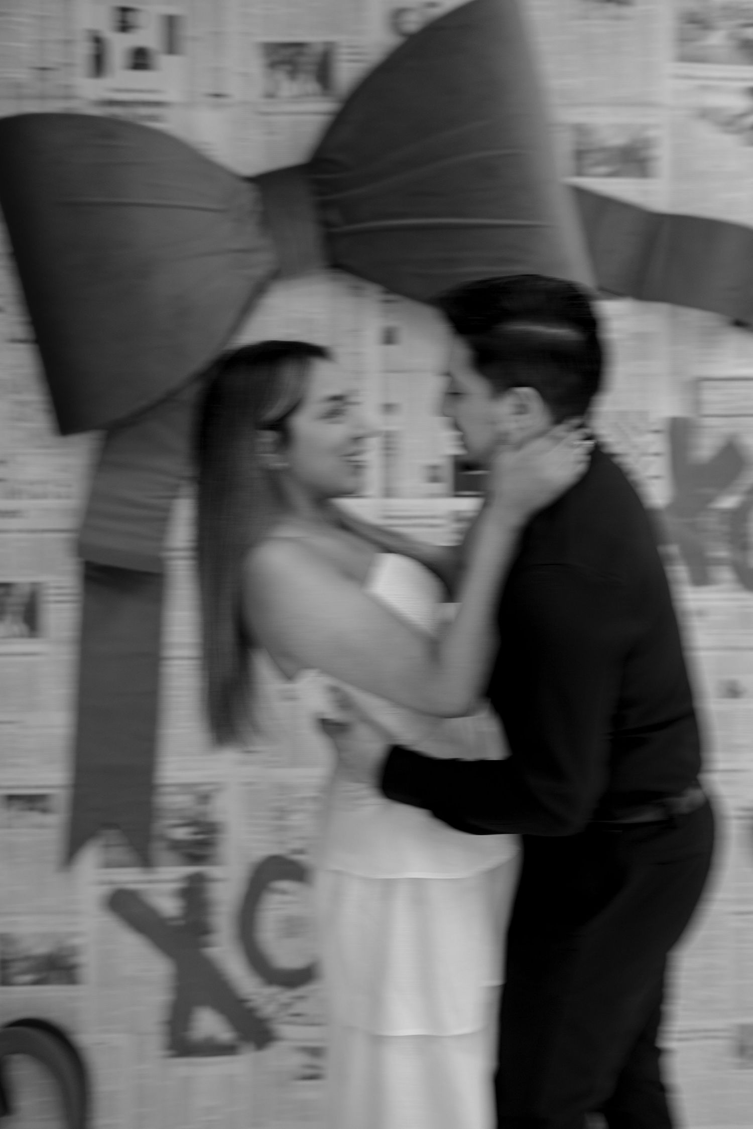 Black and white photo of couple about to kiss in front of newspaper backdrop with large bow.