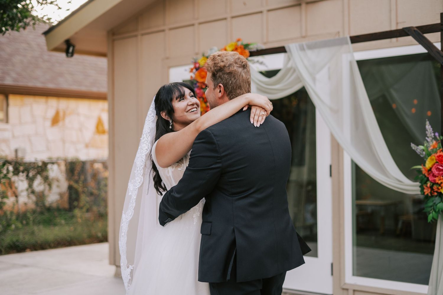 Bride and groom share emotional first look embrace outside decorated wedding venue.