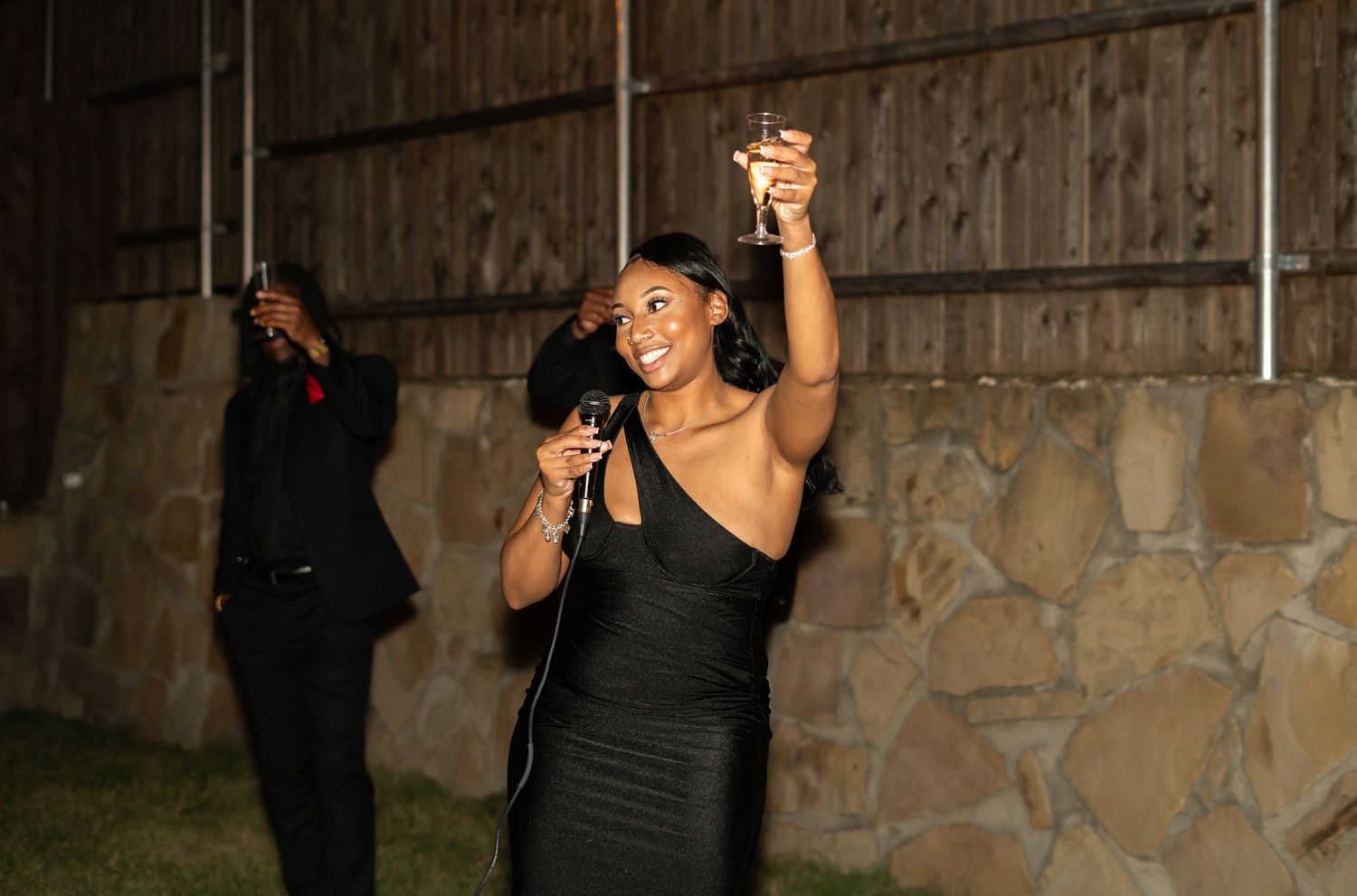 Woman in black dress dancing and raising a champagne glass at an outdoor evening celebration.