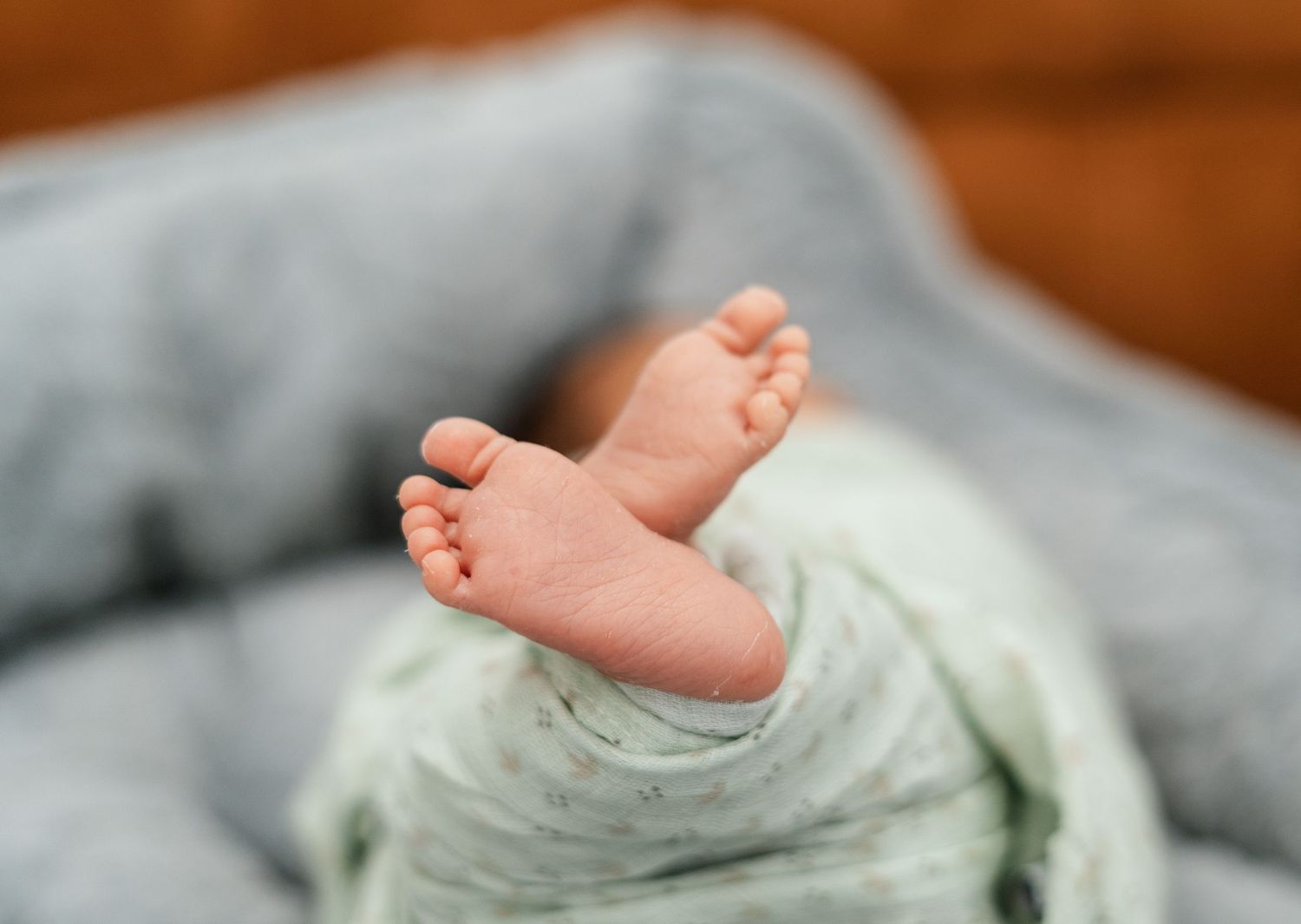 Close-up of tiny newborn baby feet peeking out from a soft green swaddle blanket.