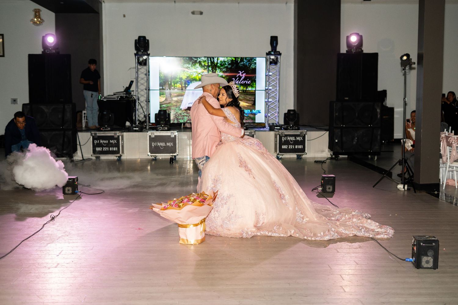 Quinceañera father-daughter first dance on foggy dance floor with pink lighting and sparklers at elegant venue.