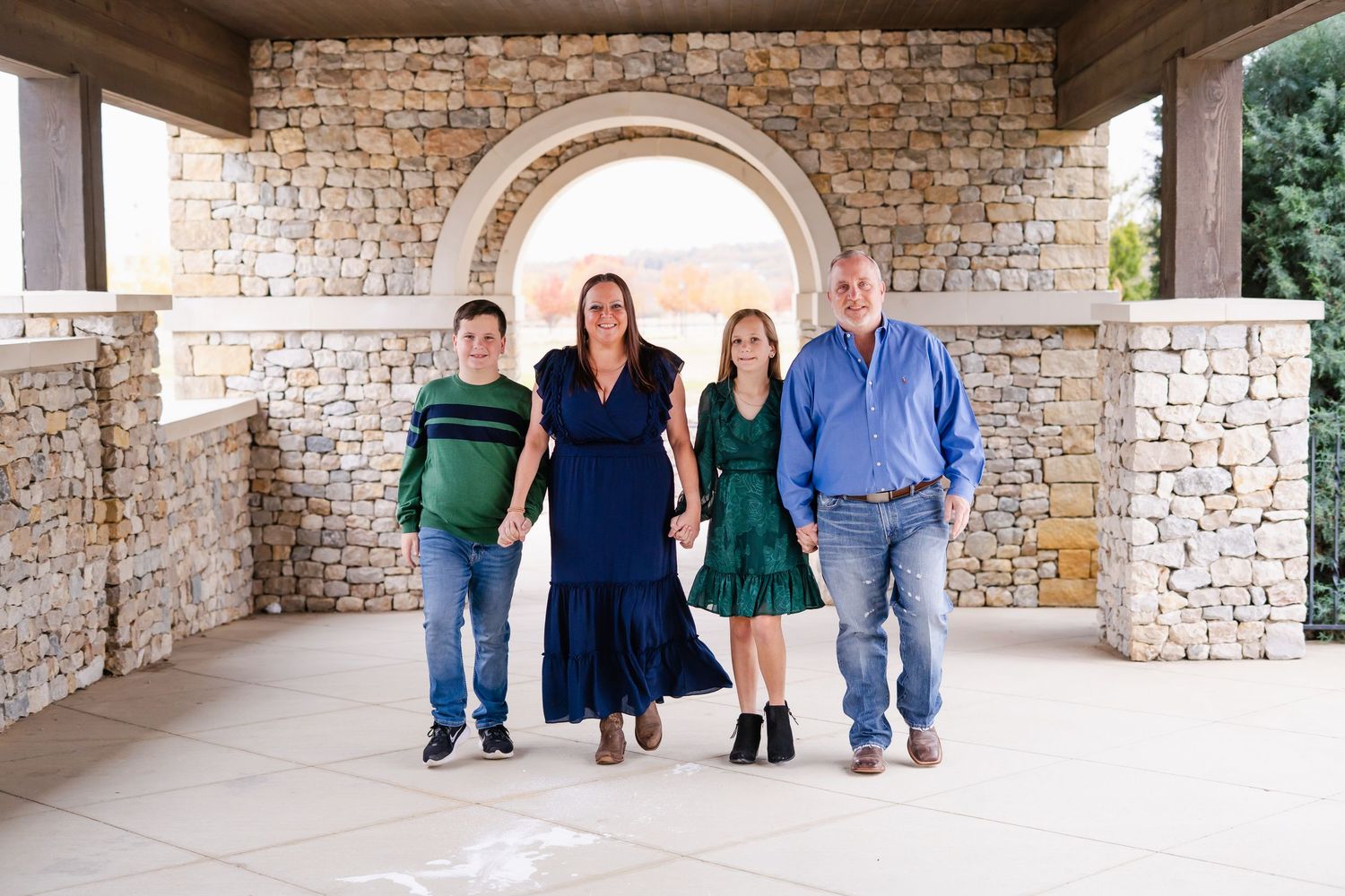 A family of four walks hand in hand under a stone archway at an elegant outdoor venue.