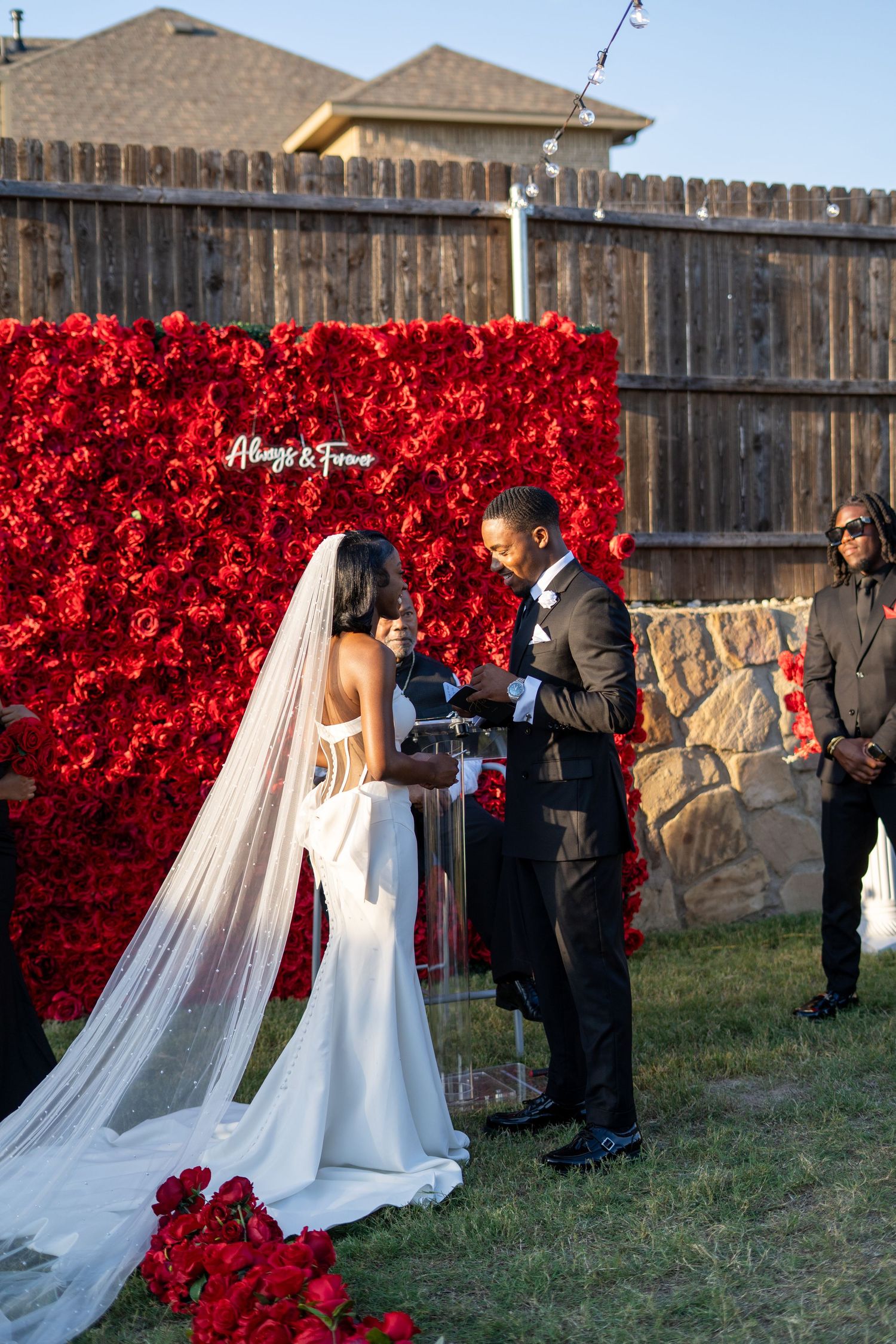 Bride and groom exchange vows before stunning red rose flower wall backdrop reading Always and Forever.