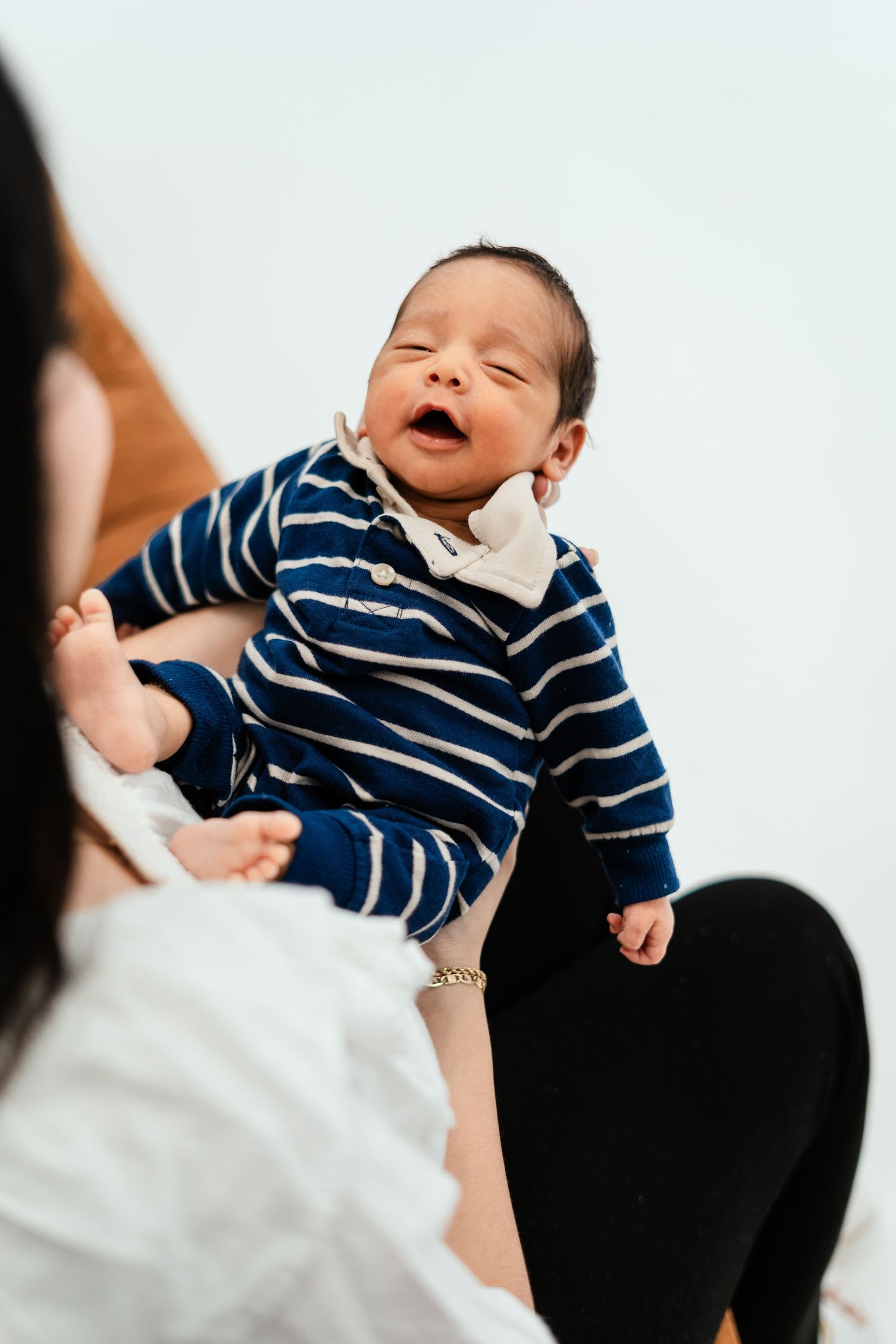 Happy newborn baby in a blue striped outfit being held up by mother during a photo session.