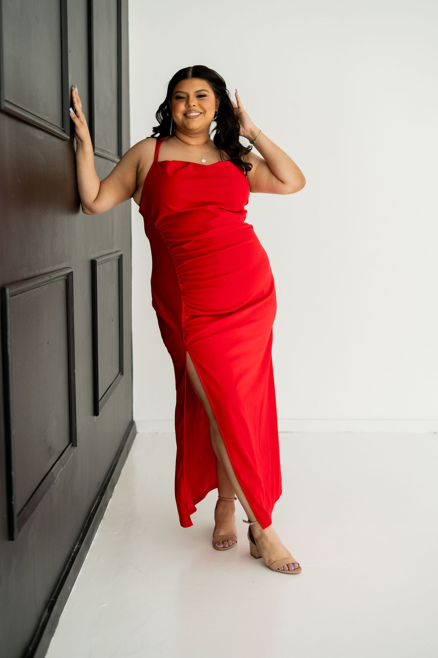 Woman in red maxi dress with slit posing against dark door in studio.