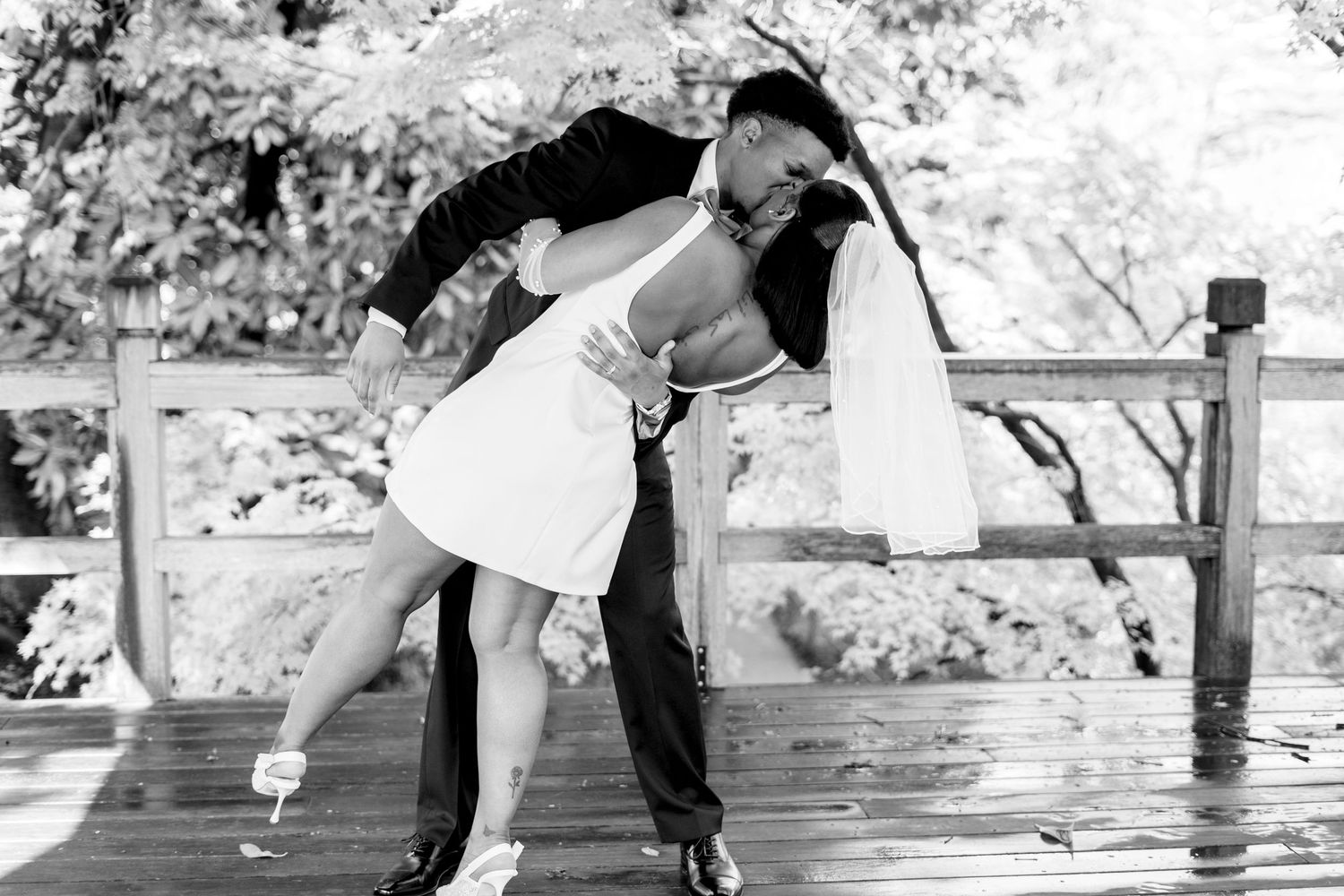 Black and white photo of a couple sharing a romantic dip pose on a wooden deck during their wedding.