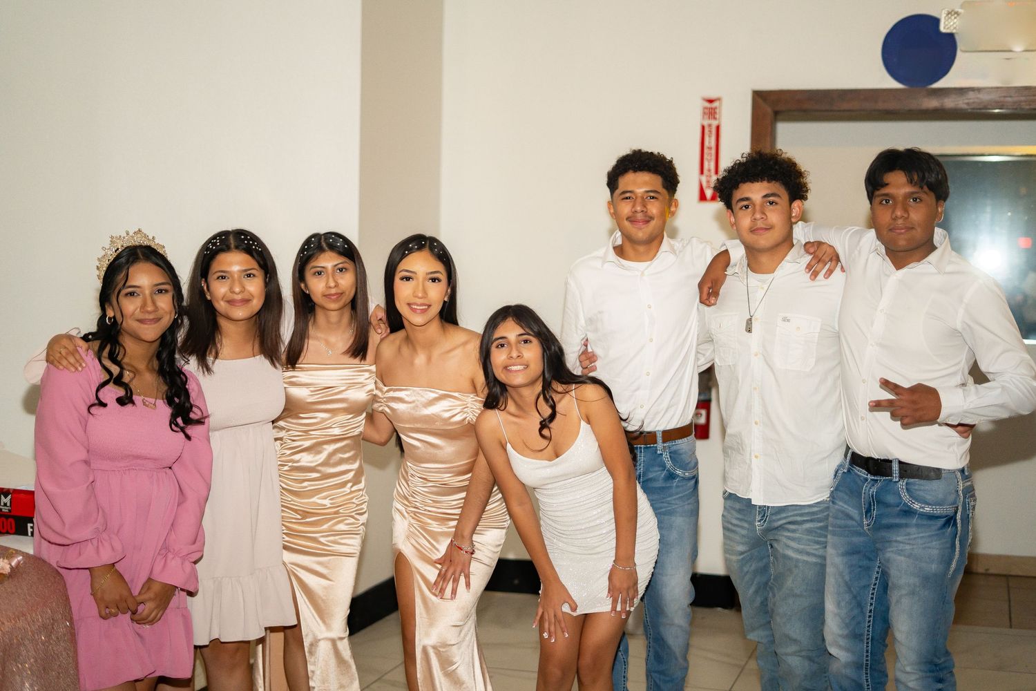 Quinceañera honoree poses with chambelanes and chambelanas in white and pink outfits at celebration.