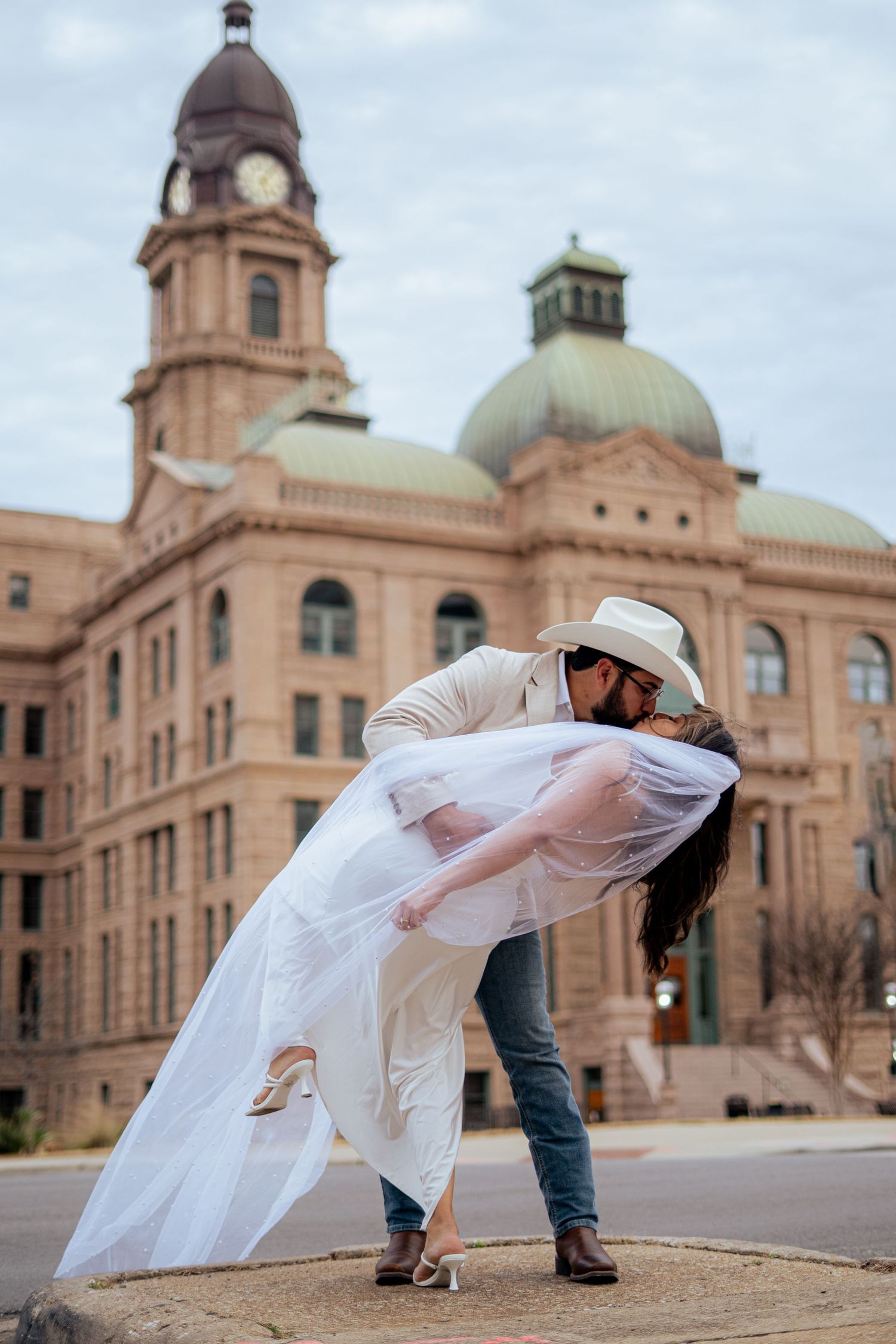 Groom dips bride in a romantic kiss in front of a grand historic Texas courthouse on wedding day.