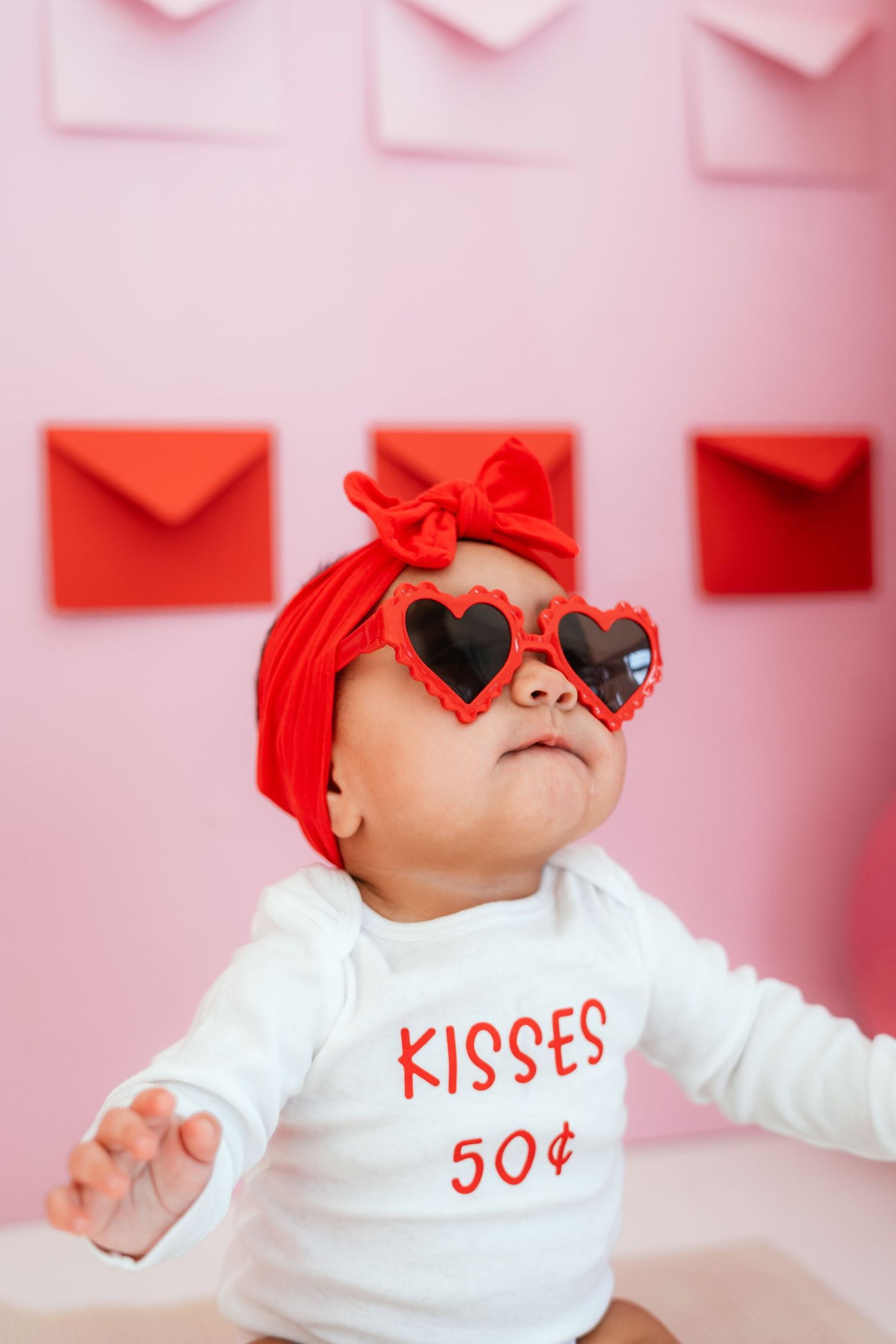 Baby in red bow and heart sunglasses wearing 'Kisses 50 cents' Valentine onesie.